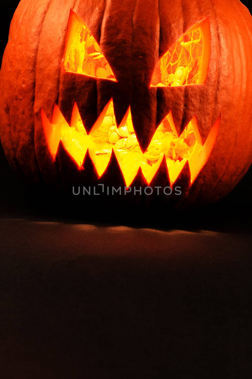 Heavy contrast photo of a carved evil pumpkin glowing.  Pulp and seeds still inside.
