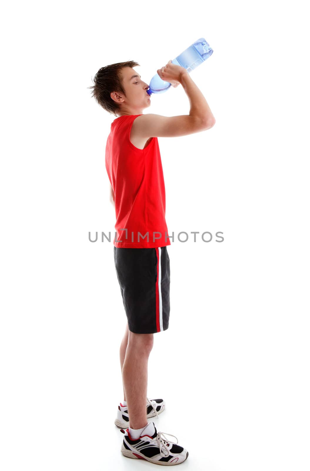 A teenage boy dressed in sports wear is drinking water from a bottle.  White background.