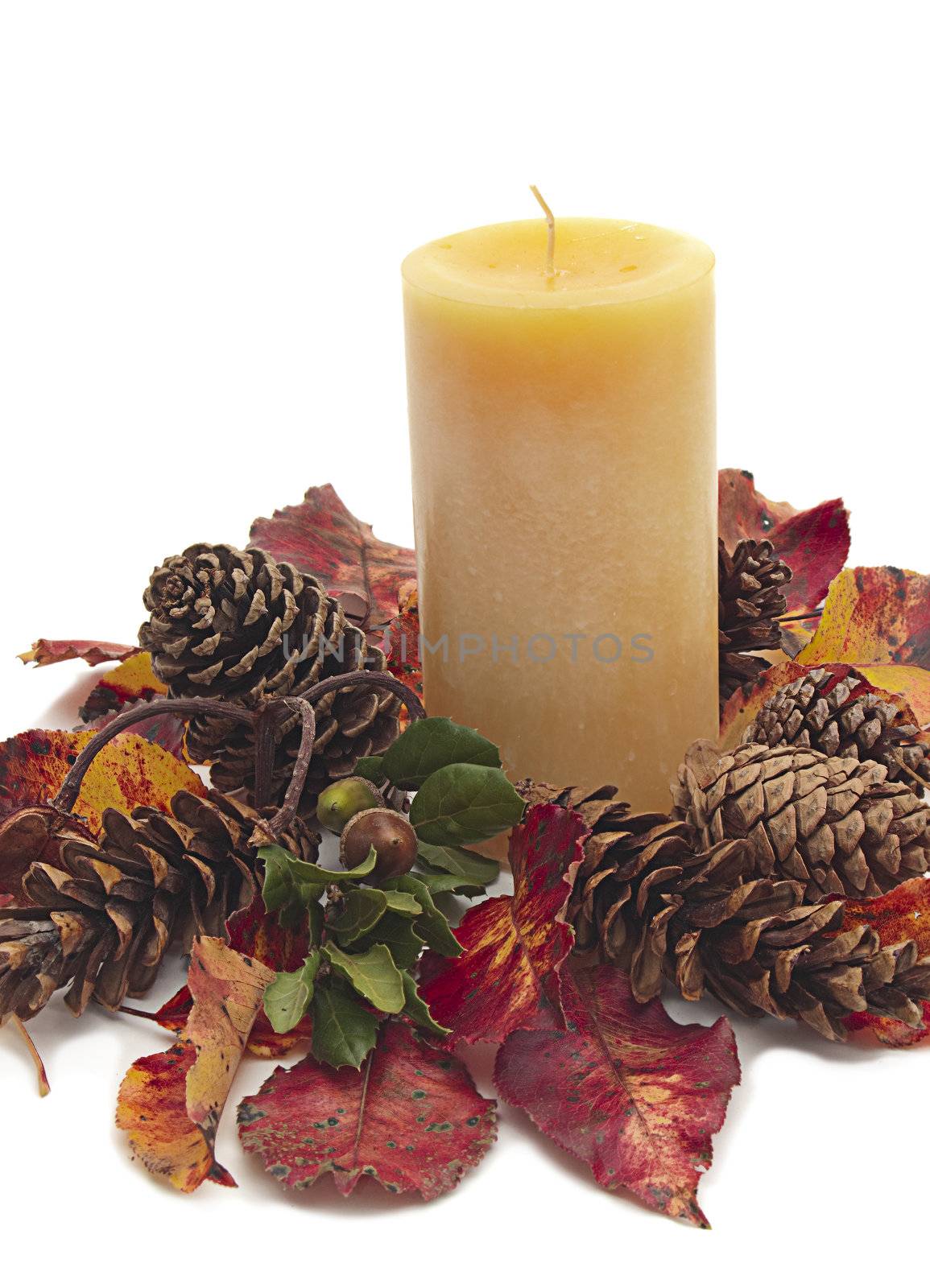 Yellow pillar candle surrounded by Fall pine cones, red and yellow leaves, and acorn on white background.