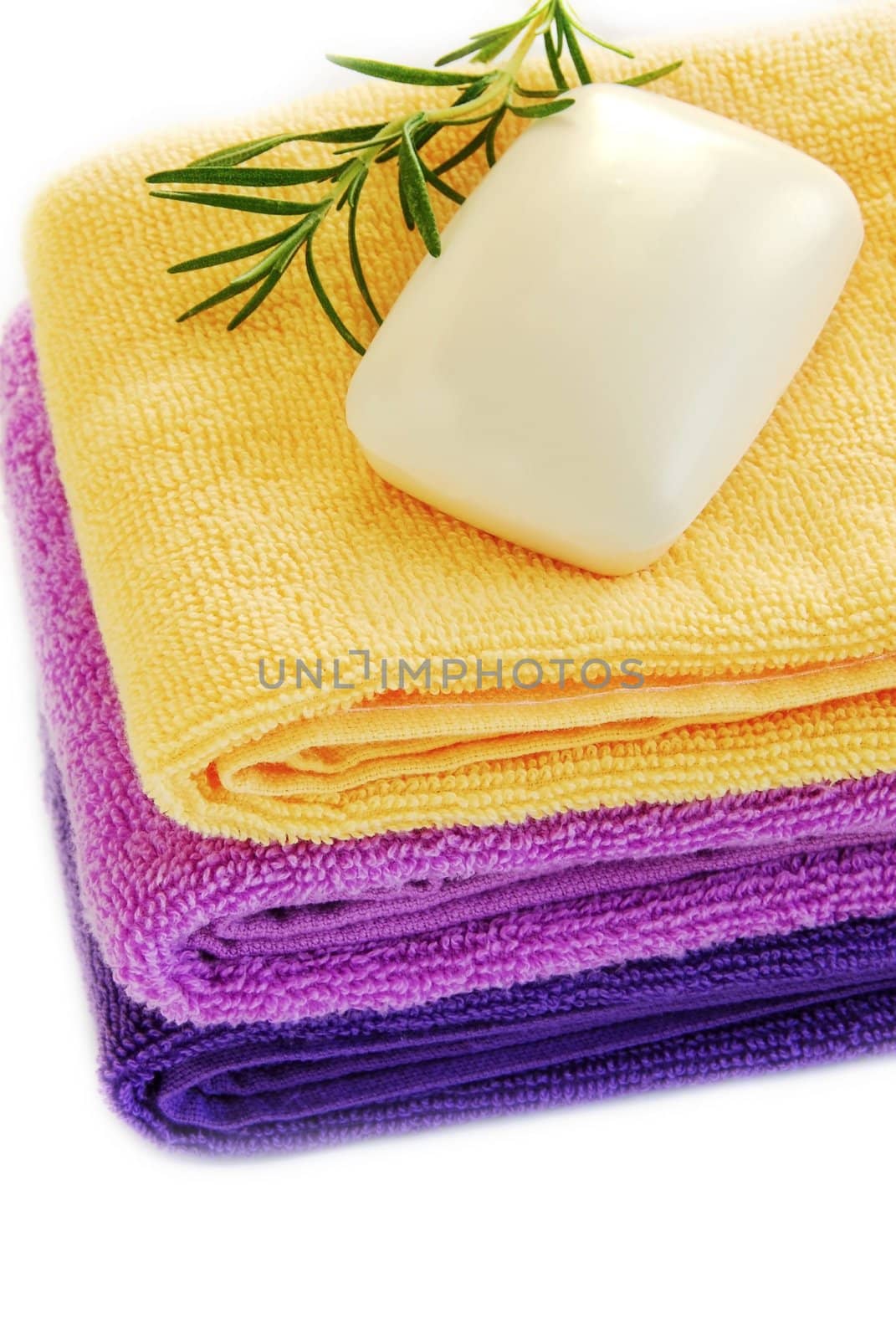 pile of colorful towels with soap and rosemary sprig over white