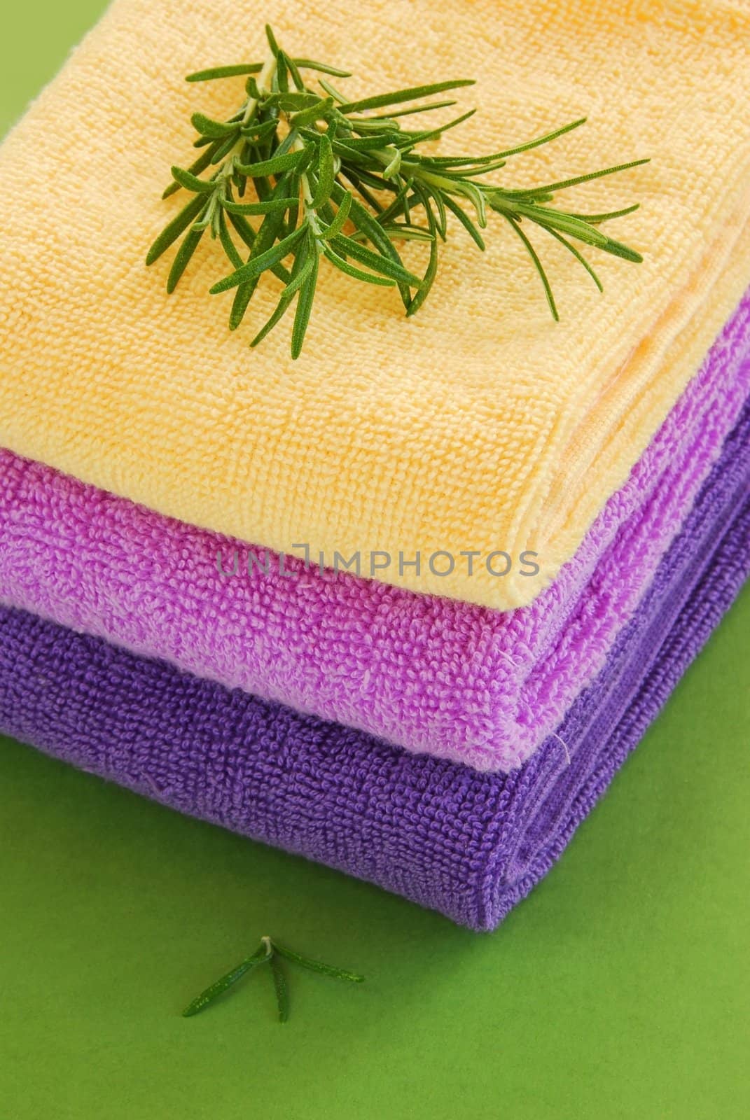 pile of colorful towels with rosemary sprig over green background