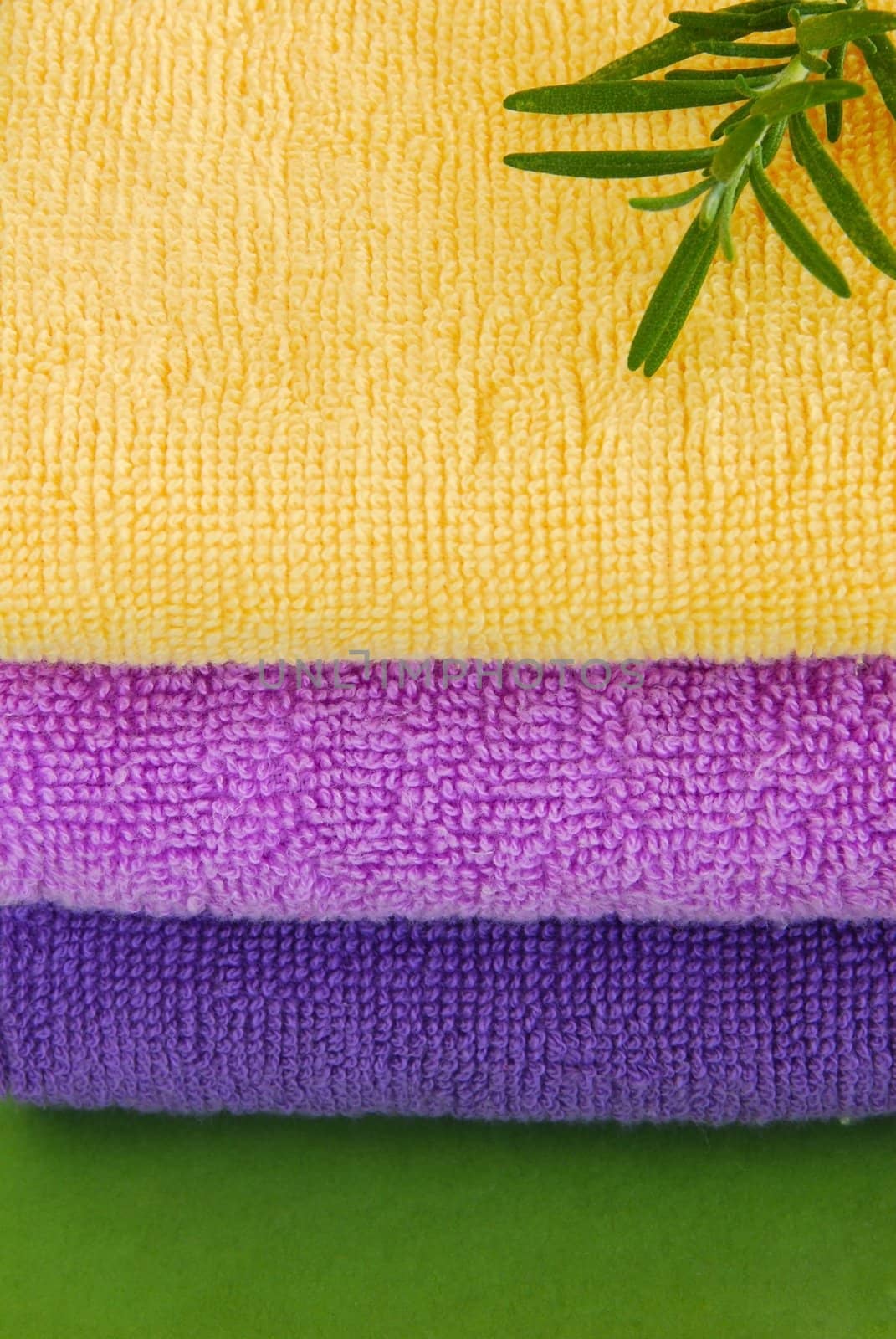 pile of colorful towels with rosemary sprig over green background