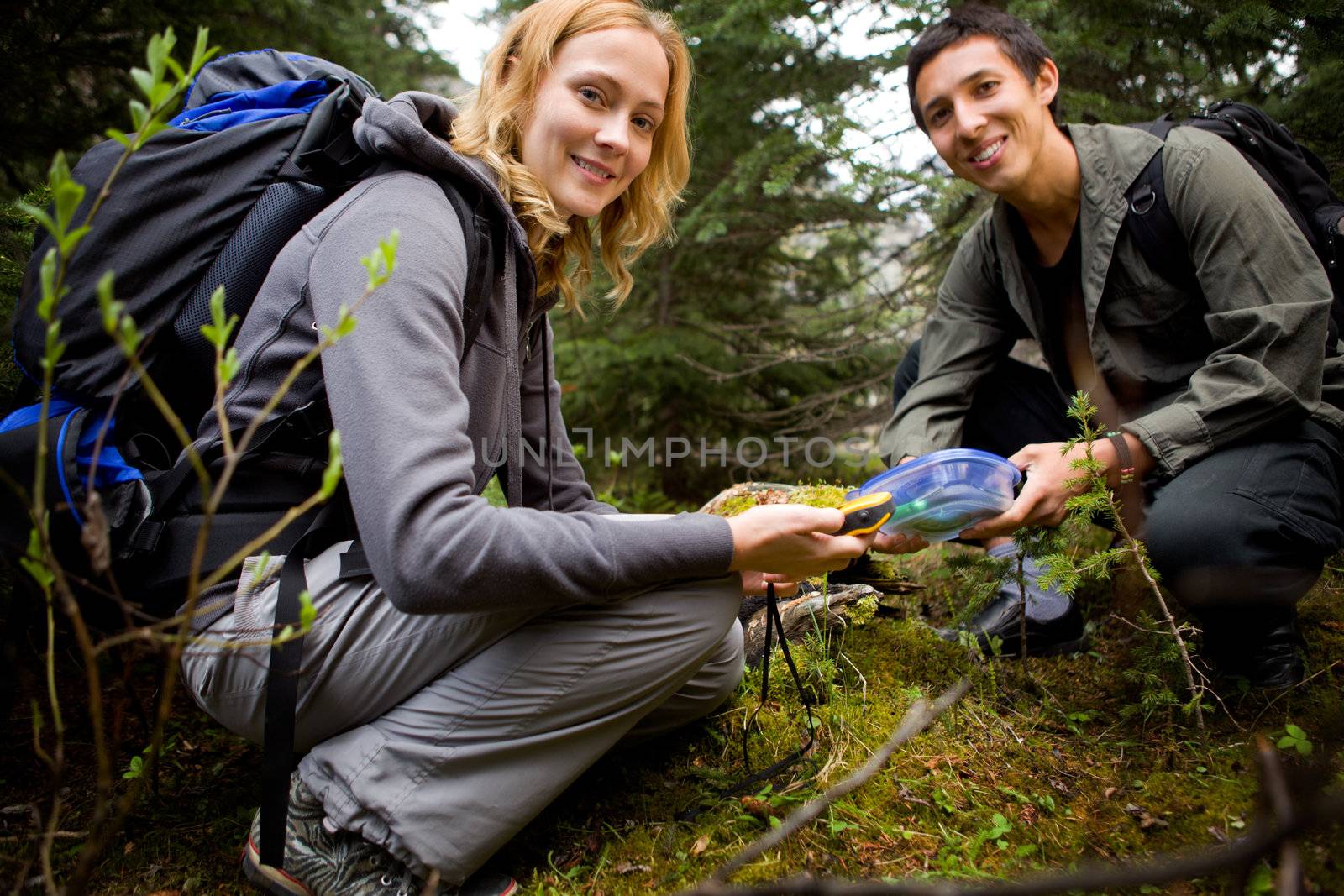 Two people finding a geocache in the forest.  Shallow depth of field with sharp focus on woman.