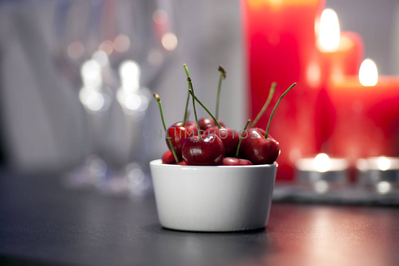 Bowl of cherries on table with candles in distance and shallow depth of field.