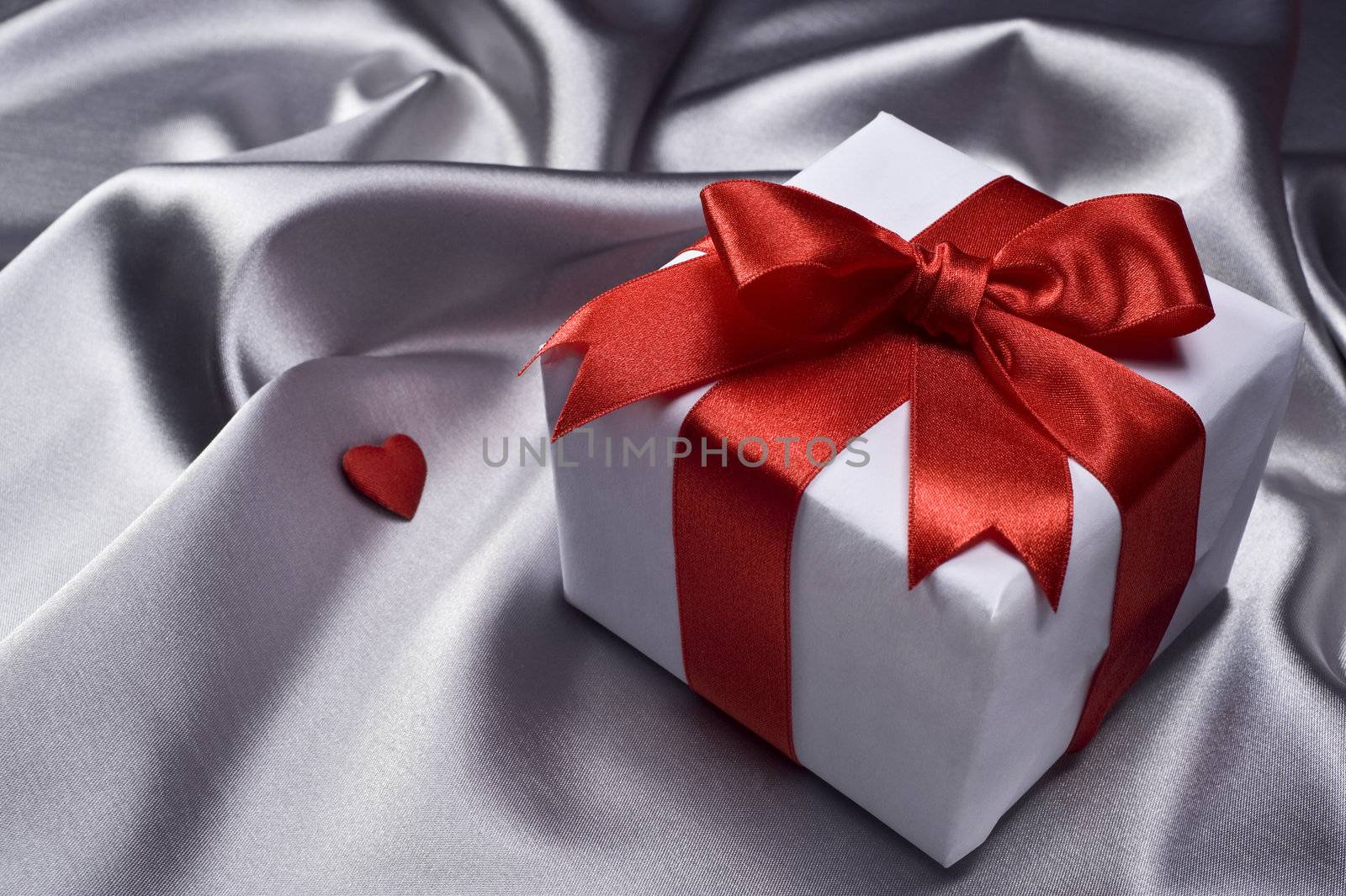 gift with decorative red ribbon on silver silk background