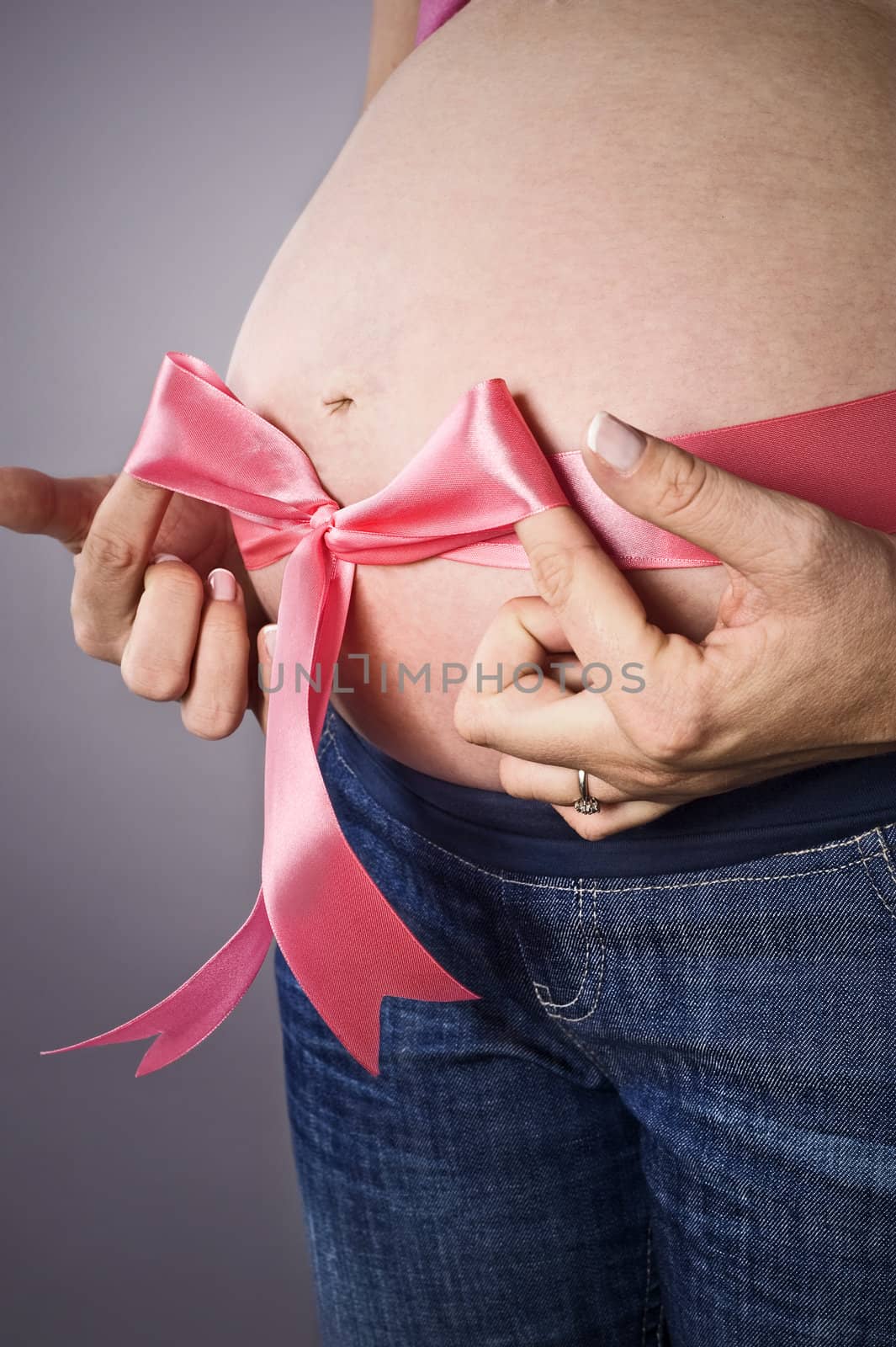 pregnant female tying pink ribbon bow on belly