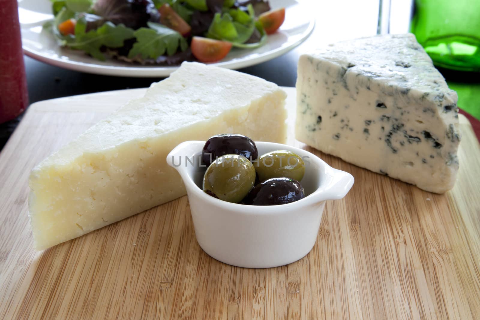 Parmesan and blue cheeses on cutting board with green and black olives.