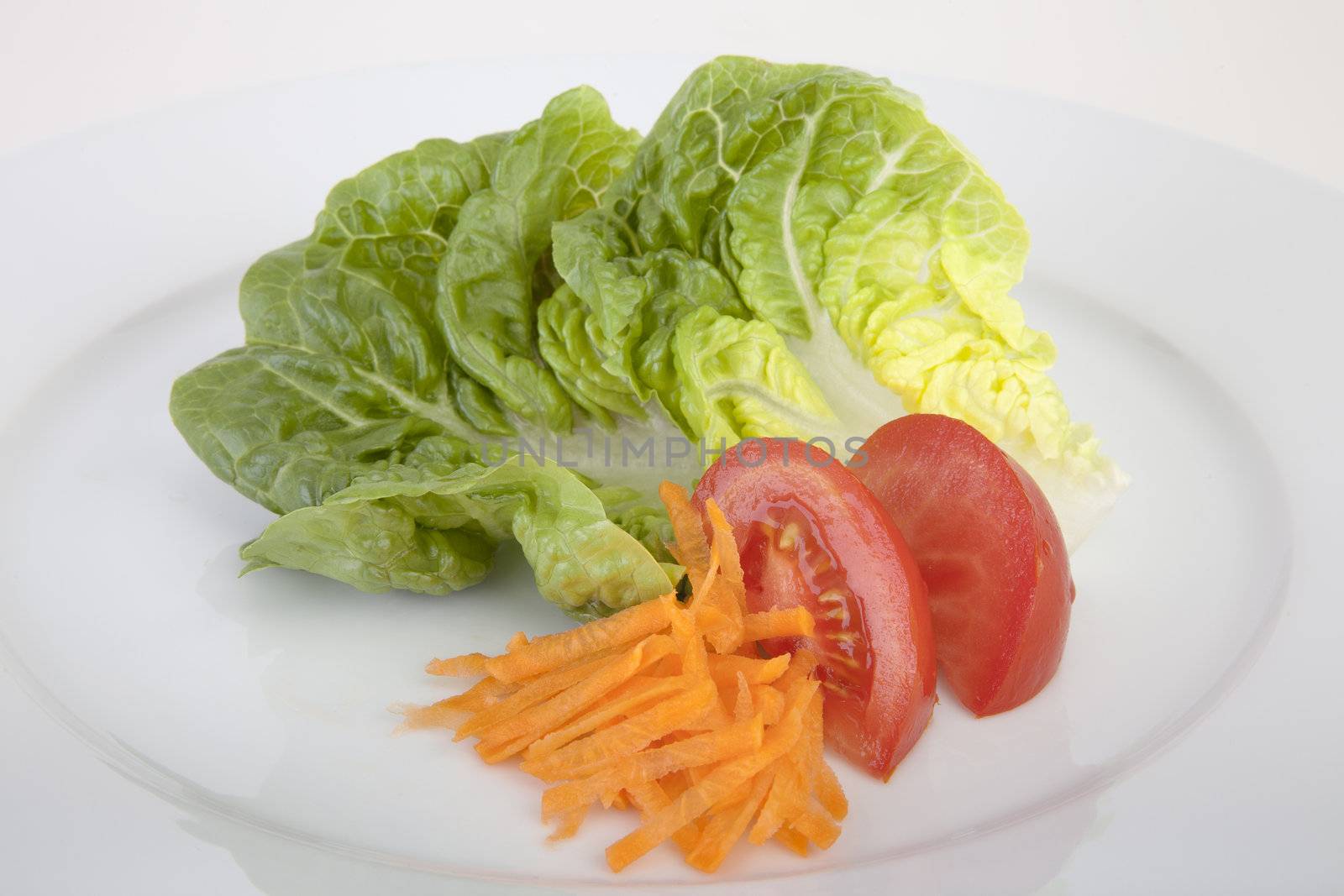 Romaine lettuce, tomato wedges and shredded carrots on white plate.