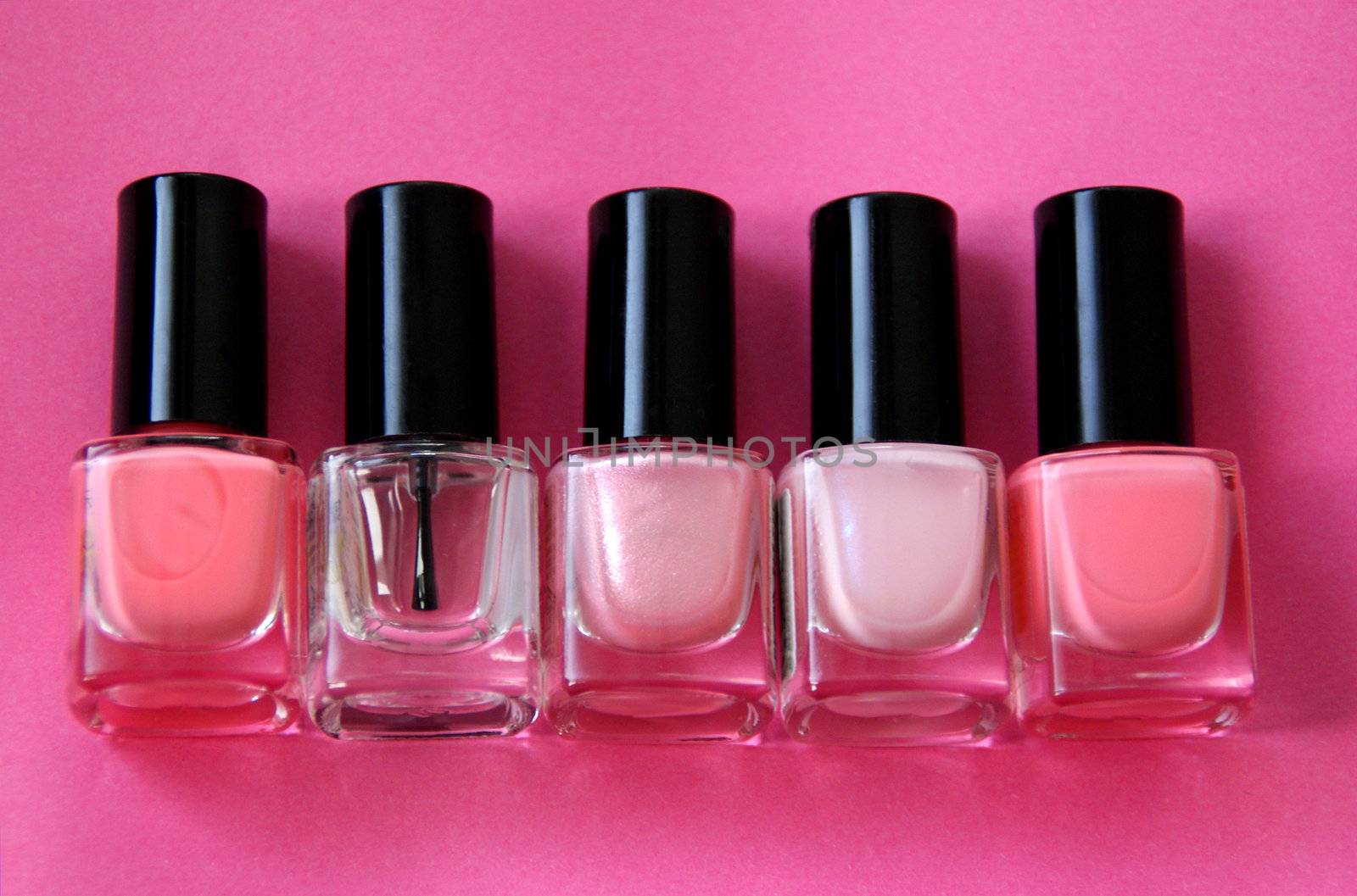 Five bottles of nail polish over a pink background.