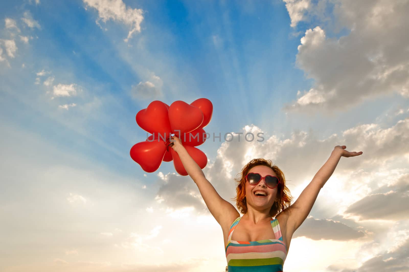 Pretty girl with heart shaped baloons over gorgeous sunset sky