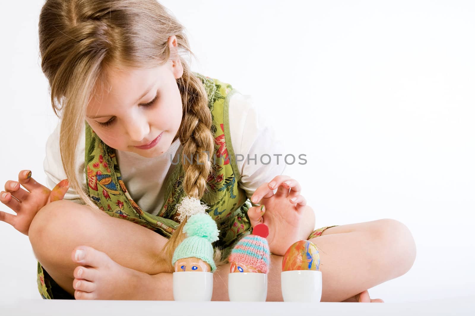 Studio portrait of a young blond girl who is checking her painted easter eggs with wool hat