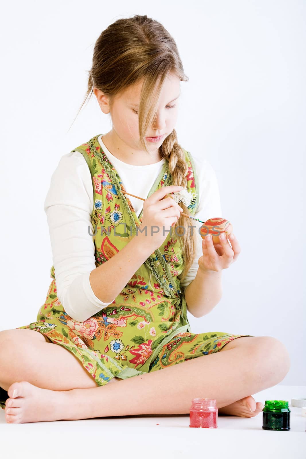 Studio portrait of a young blond girl who is concentrated on painting eggs for easter