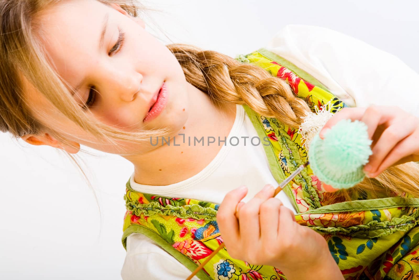Studio portrait of a young blond girl who is concentrated on painting an egg