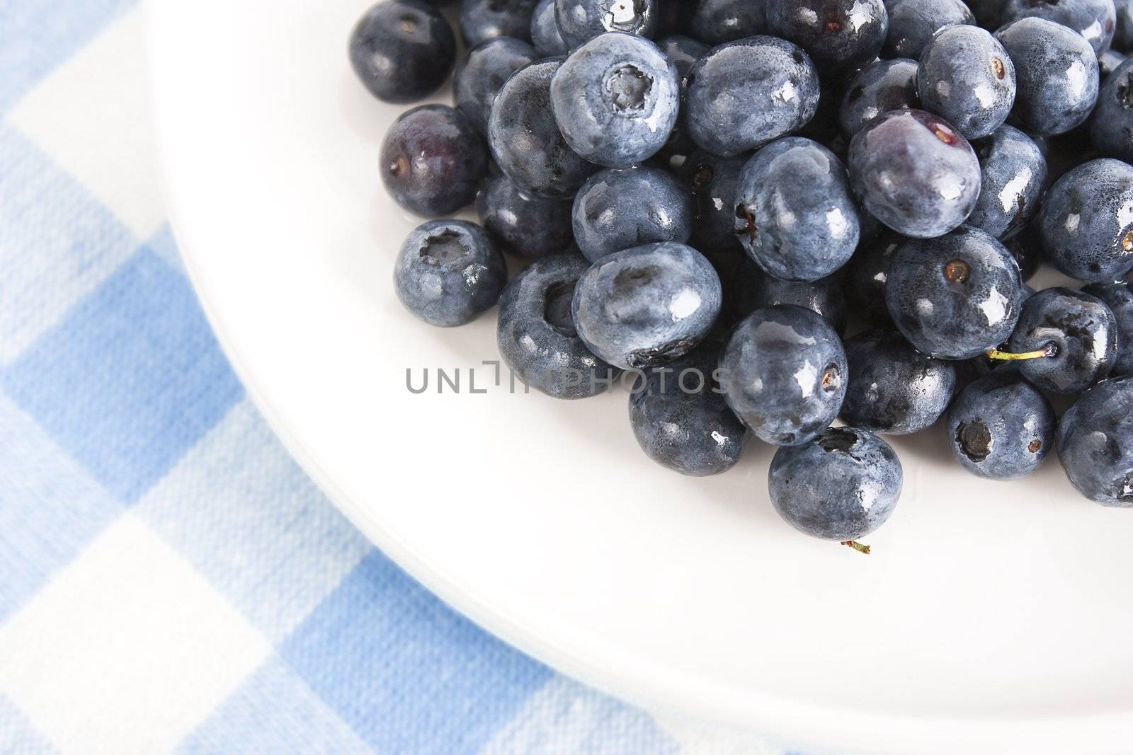 Closeup of blueberries on white plate and blue and white linen tablecloth