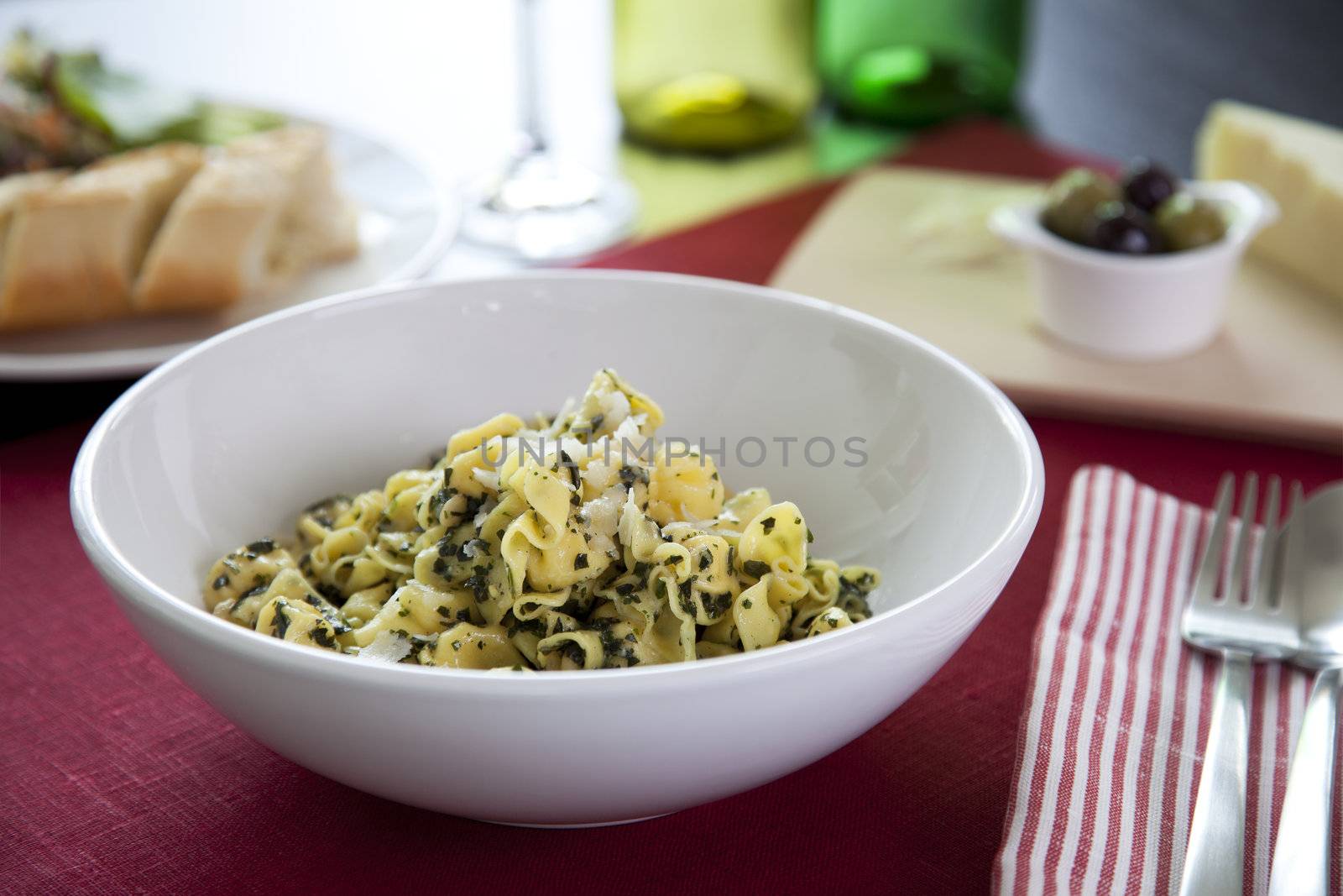 Perline pasta with pesto sauce on table with salad and olives.