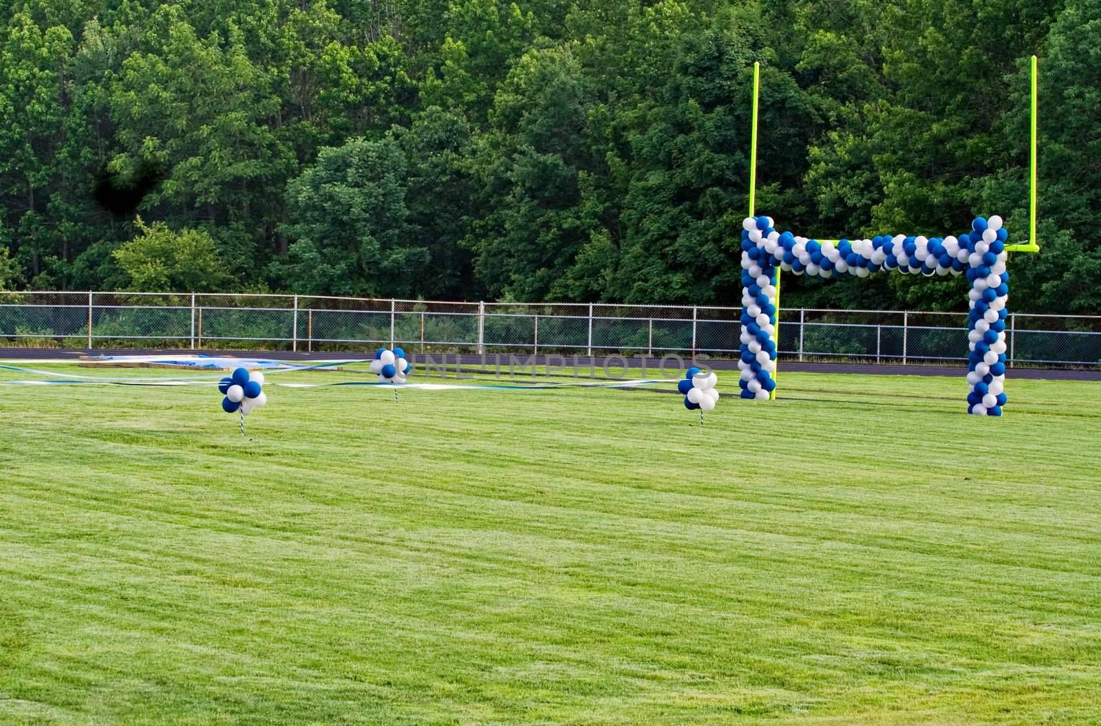 A High School football field with goal posts decorated with balloons. The field decorations are preparations for a graduation ceremony.