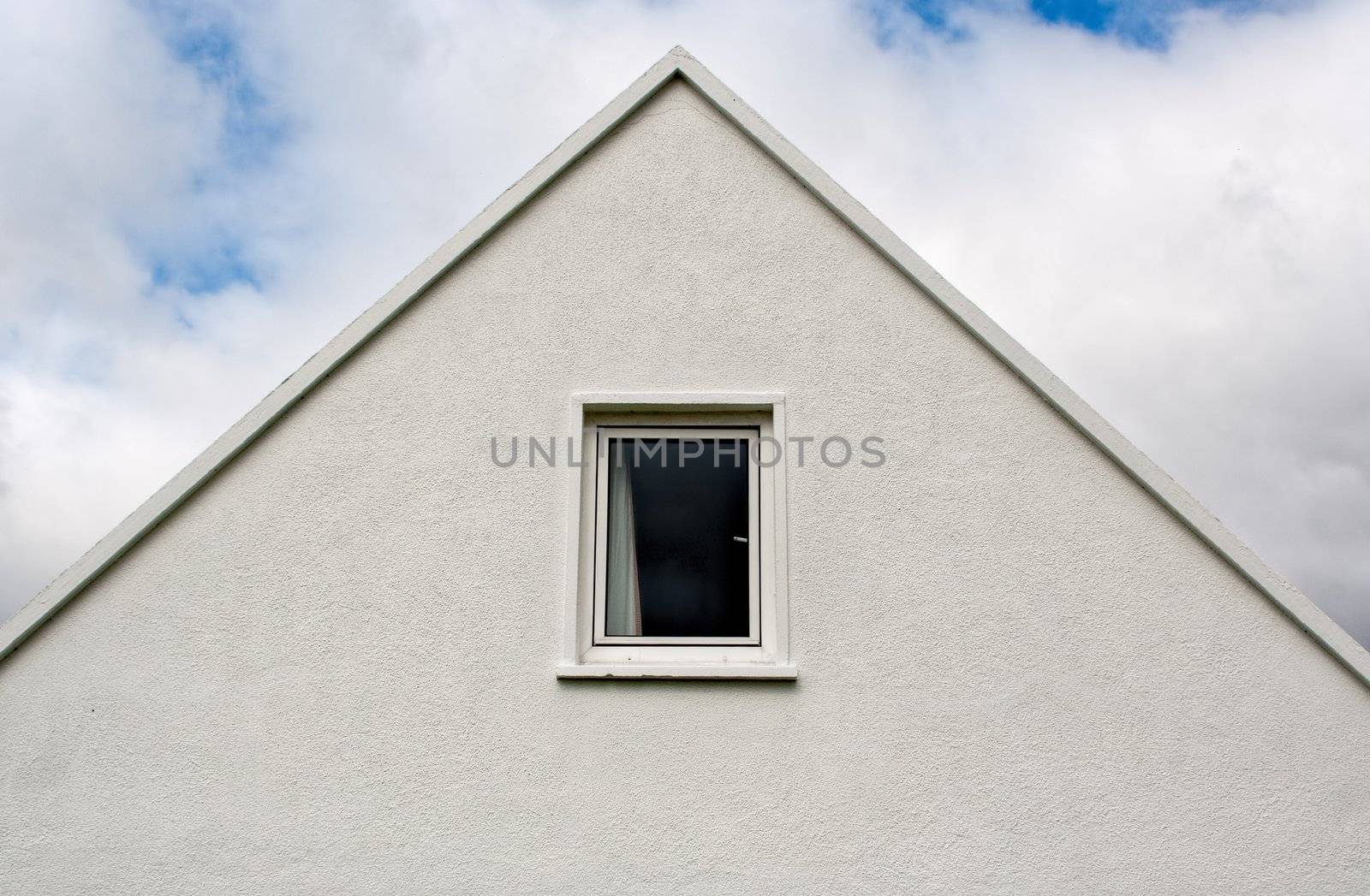 An abstract image of the top of a house. The house forms a triangle against a cloudy sky.