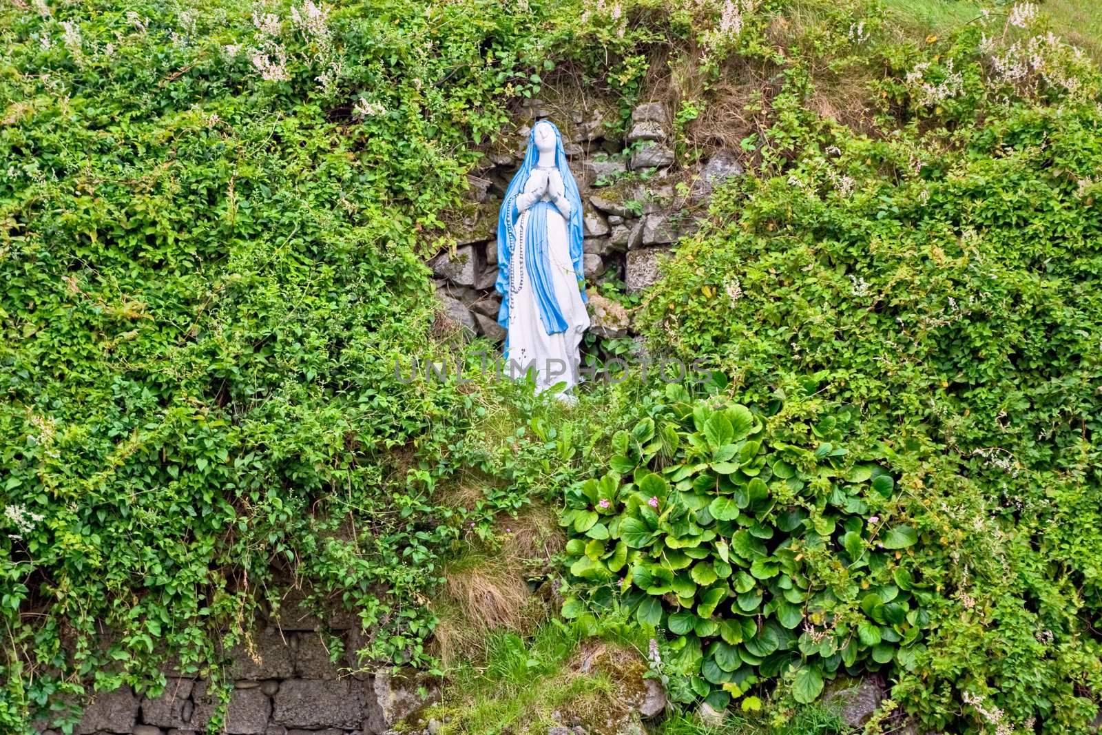 A statue of Virgin Mary on a hill surrounded by foliage