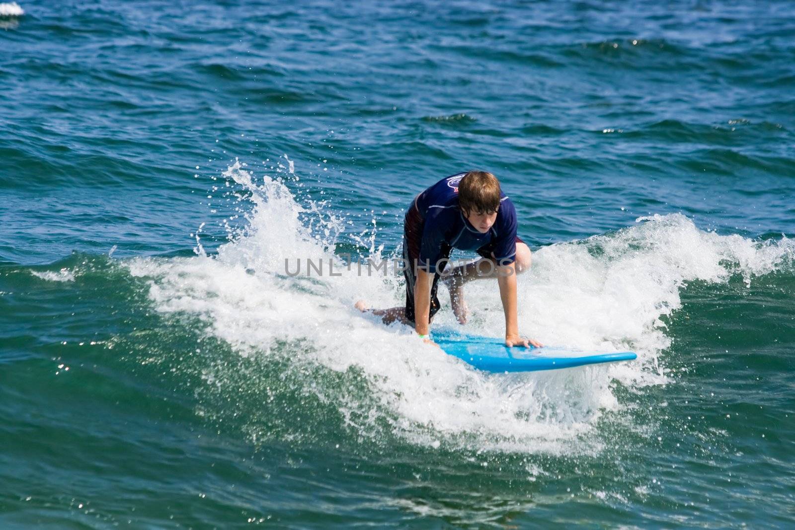 A teenager surfing. The boy is just beginning to stand up on the surfboard.