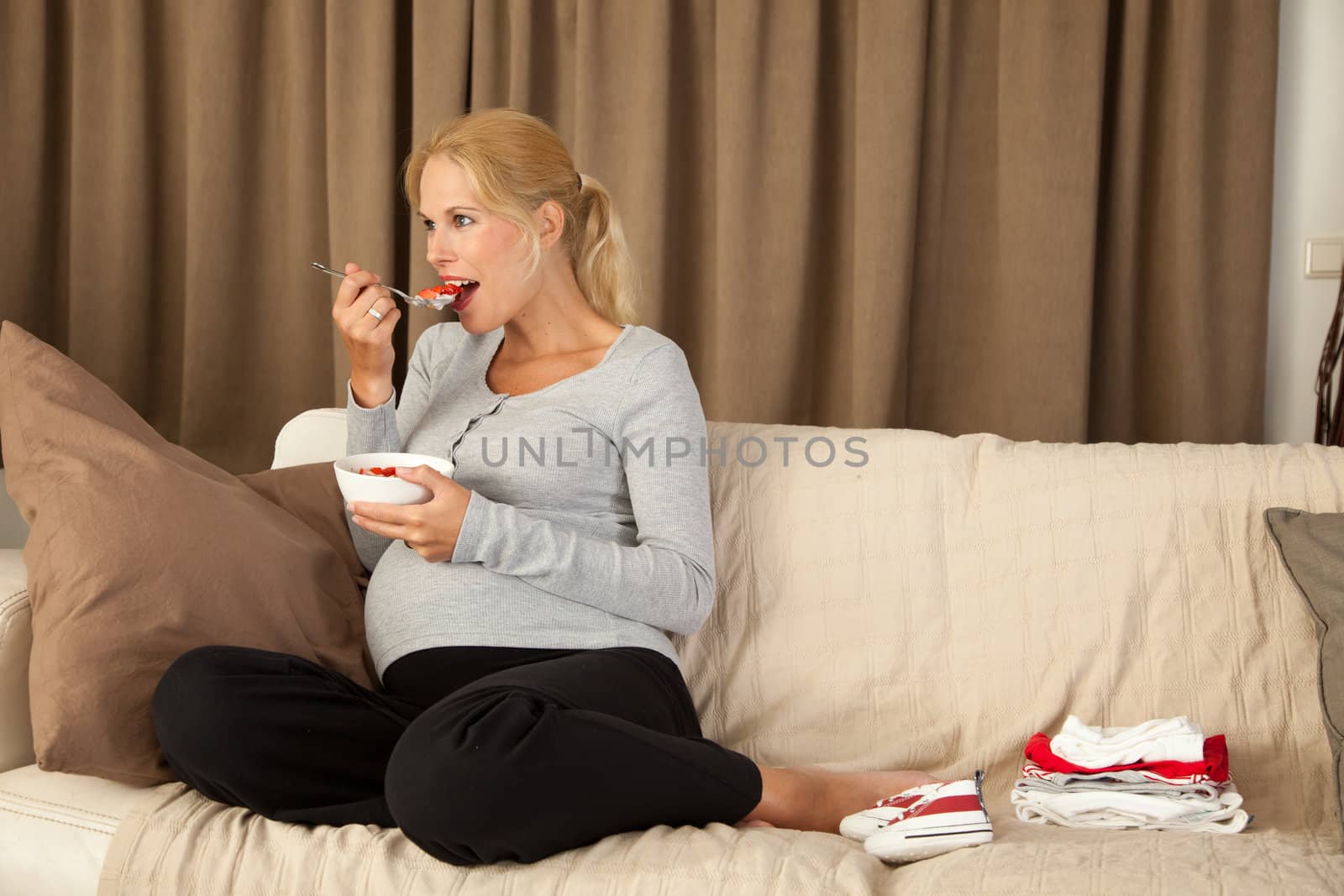Beautiful pregnant woman eating a healthy lunch sitting on the couch