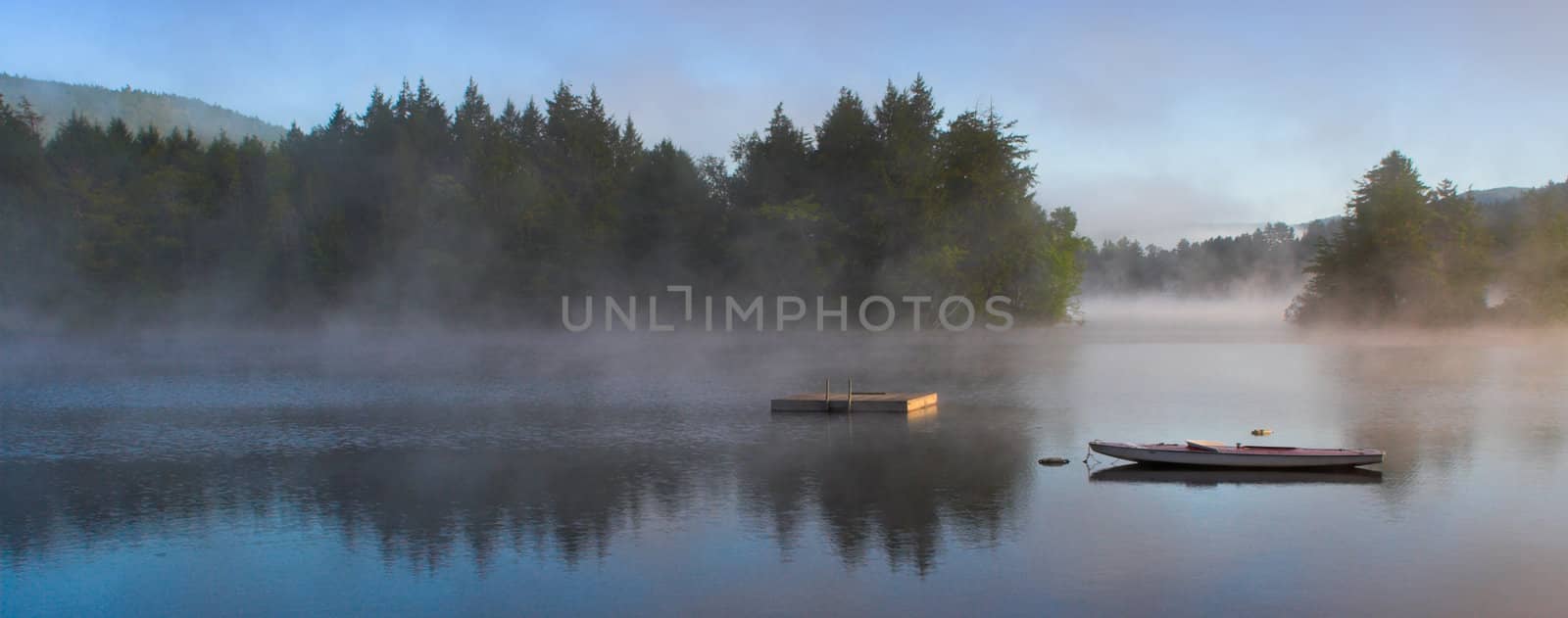 A lake in the early morning with rising fog. Panorama format.