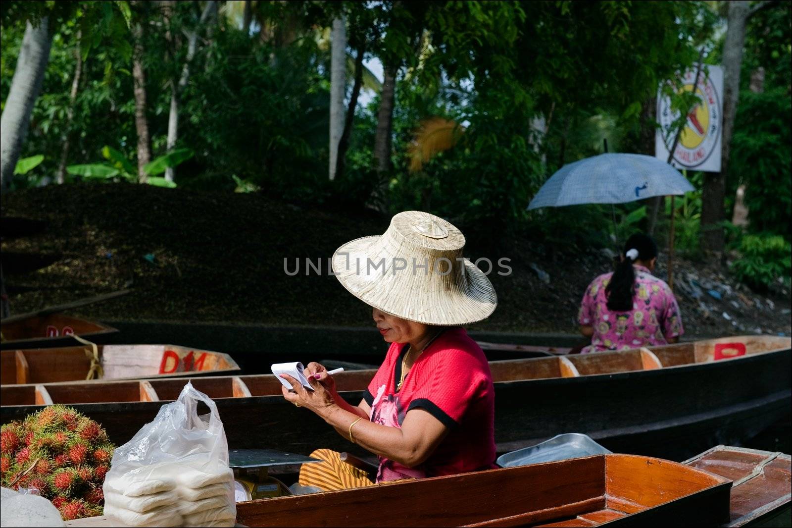 The seller by a boat. The seller of vegetables and fruit floats by a boat on the channel.