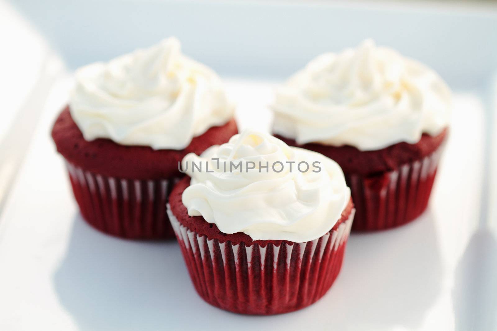 Three red velvet cupcakes on a white dish with extreme shallow DOF.