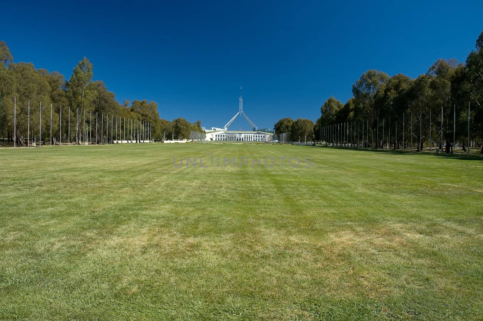 Canberra Parliament House in distance, green grass in foreground, clear blue sky