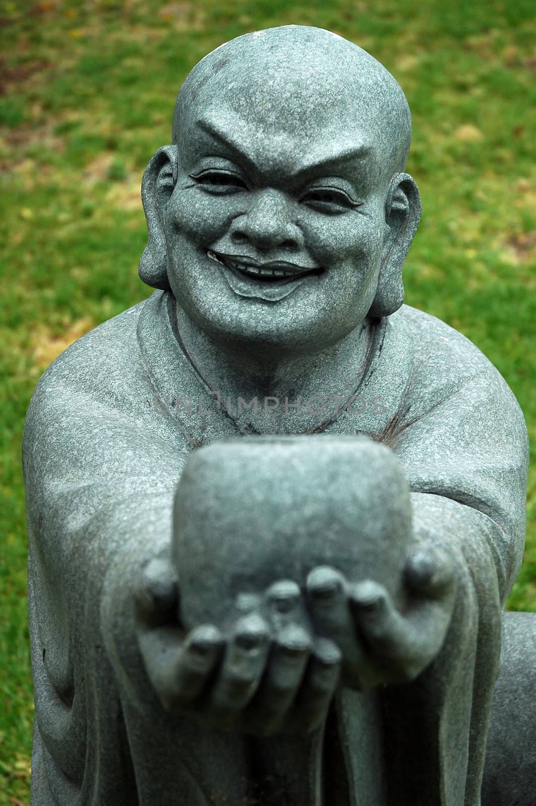 stone buddha sculpture offering a cup and smiling, grass in background