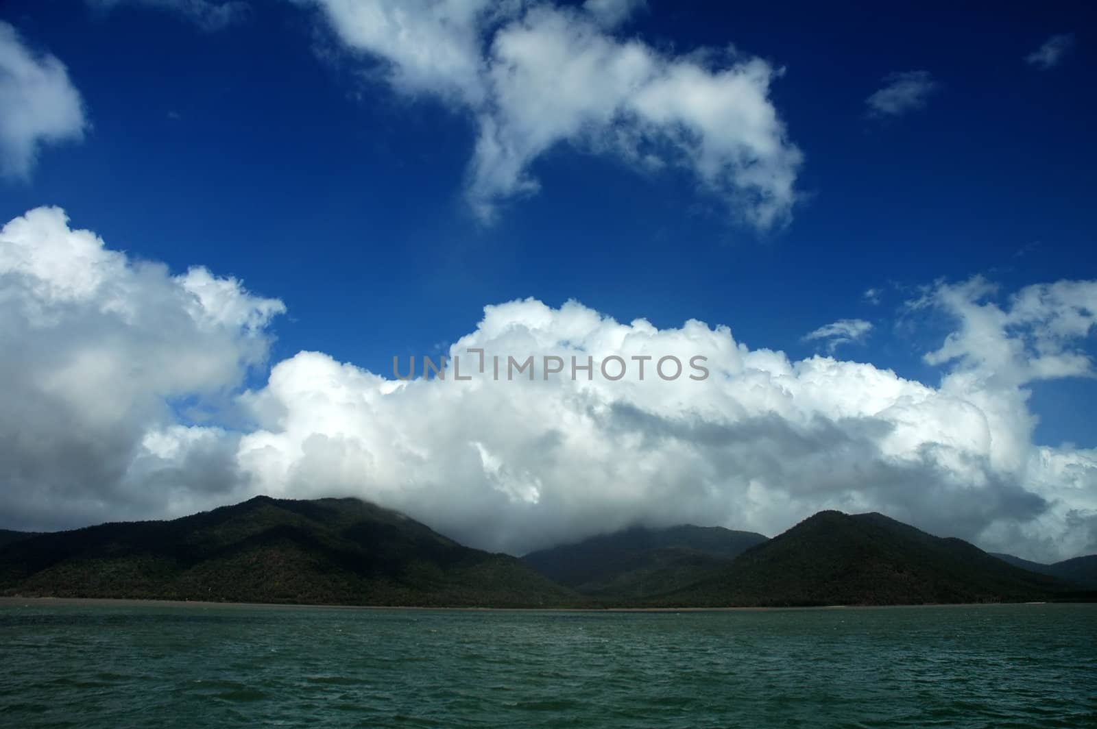 green ocean, green forest mountains, dark blue sky, clouds, ocean view, photo taken near Cairns