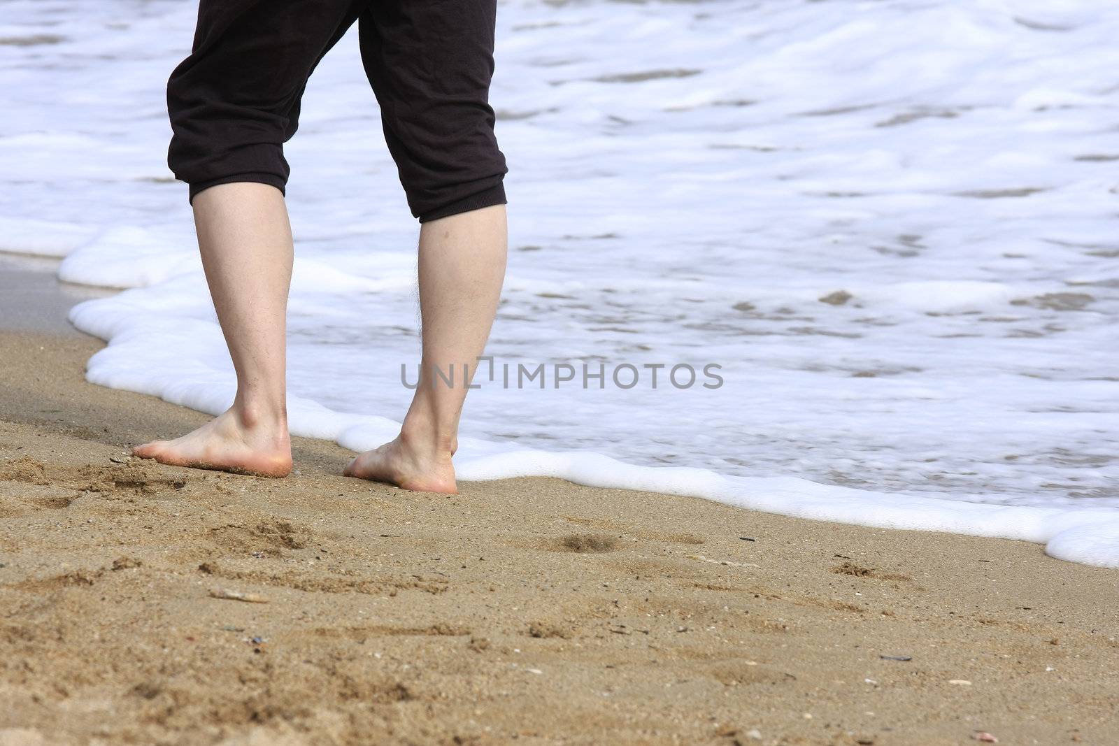 Man standing on a sandy beach with waves at her feet
