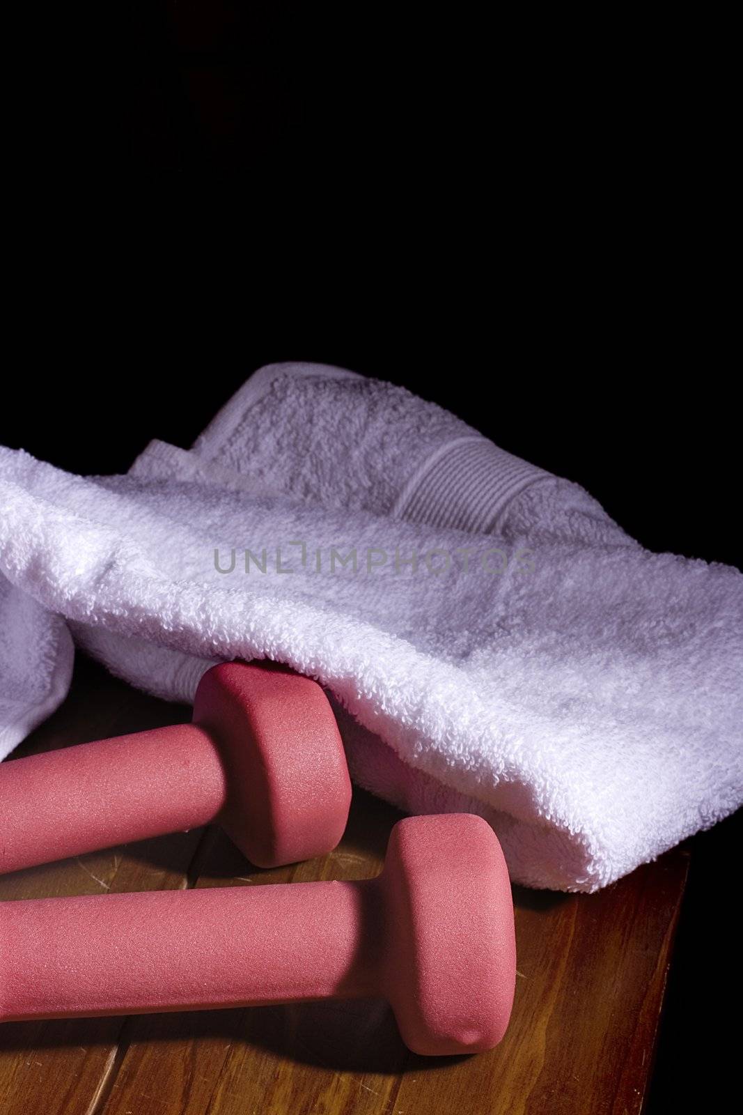 Two pink dumbbells laying next to a white towel on a wooden surface.