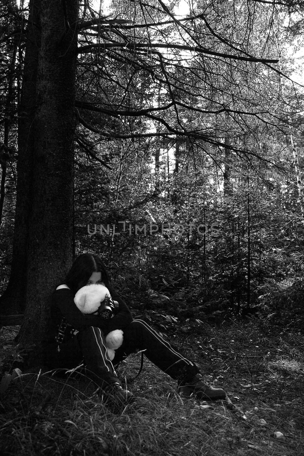 black and white portrait of a twenty something girl dress in goth fashion with a white teddy bear wearing a gaz mask, while being scared lost in the woods