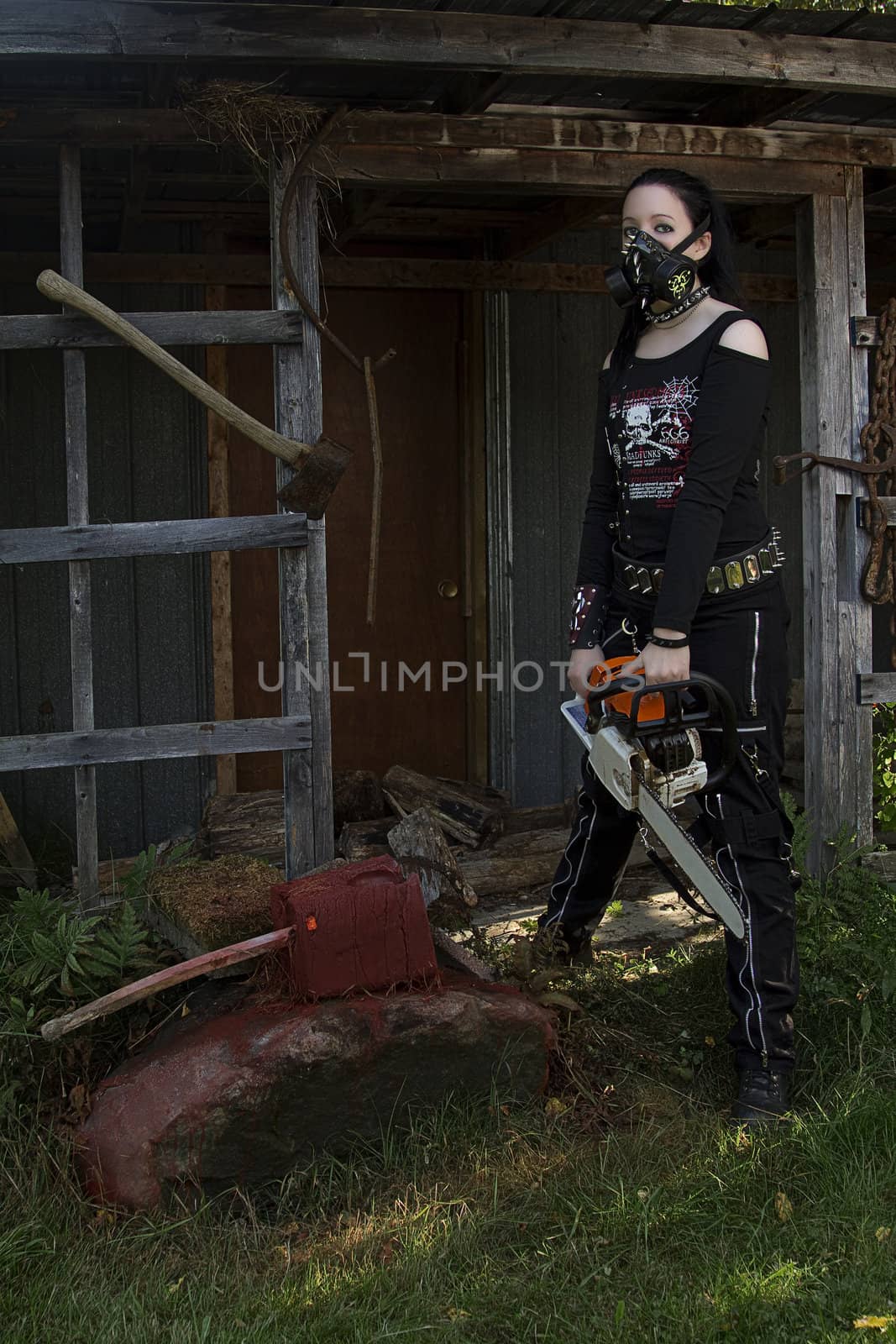 twenty something girl dress in goth fashion with a chainsaw in front of a abandon shack