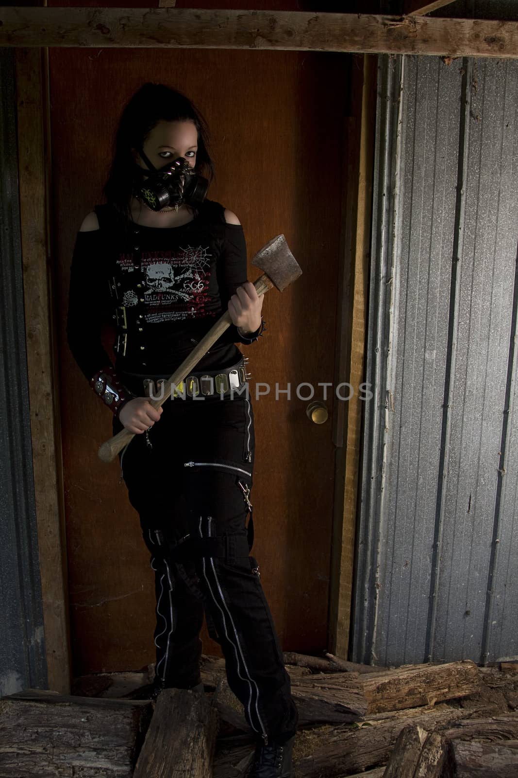 twenty something girl dress in goth fashion with a axe in front of a wooden door