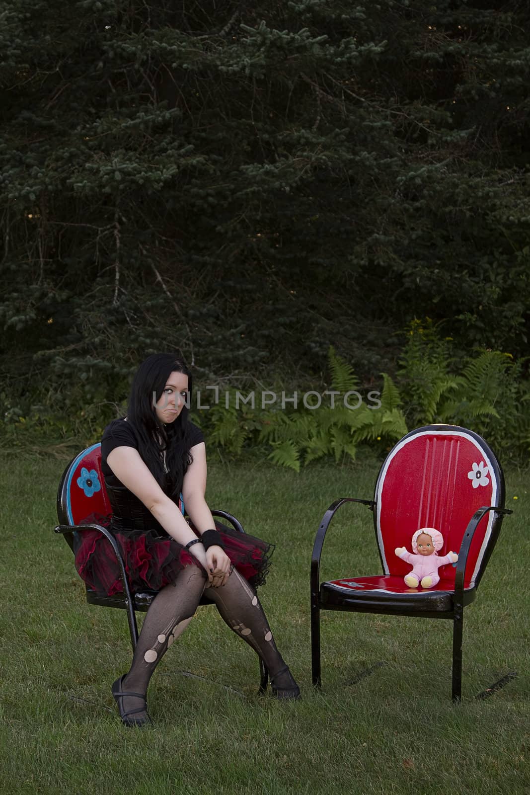 early twenty women wearing goth style clothes sitting on a lawn chair with her baby doll sitting in a lawn chair beside her