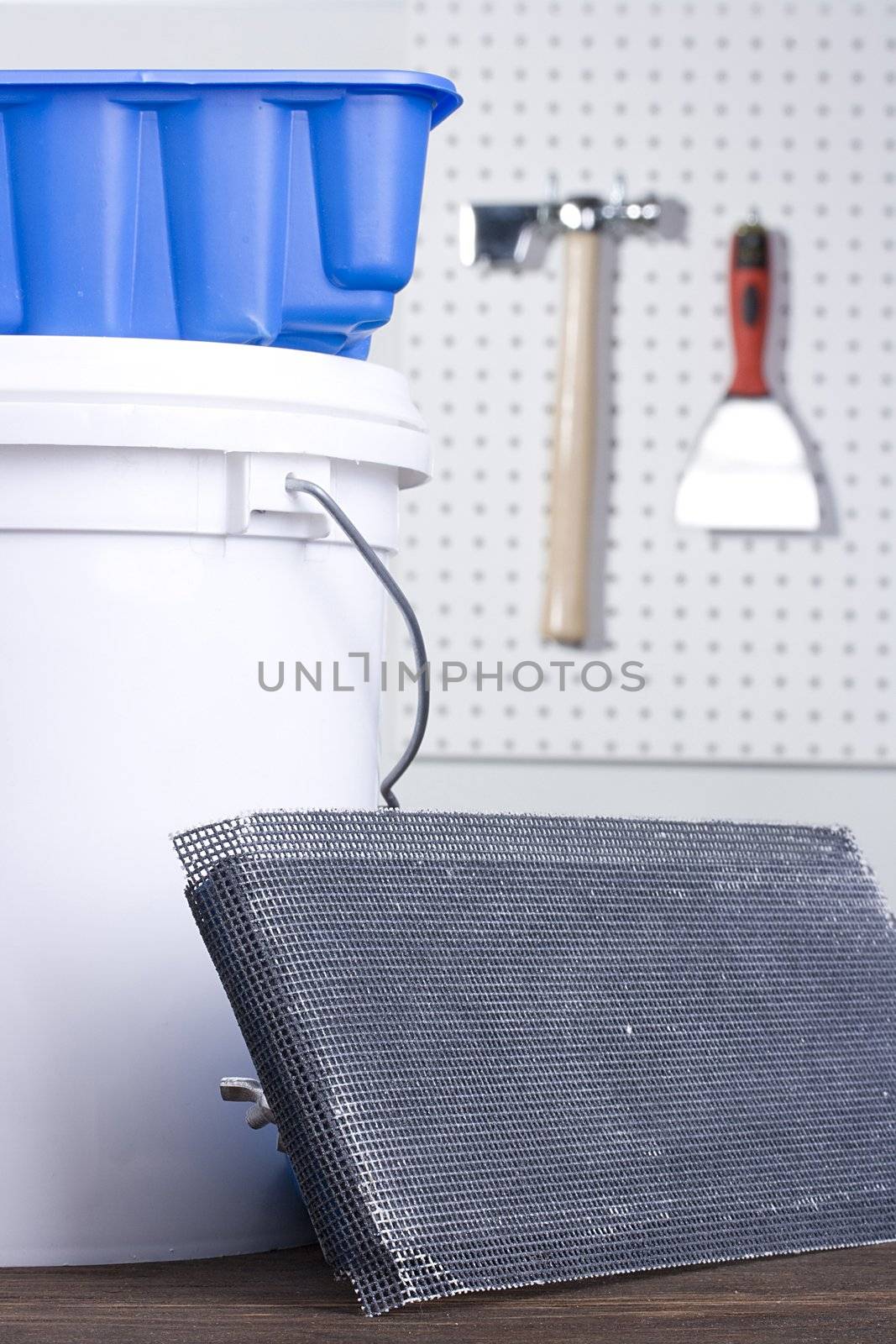 Plastering trowel next to a white bucket and a blue plaster holder.