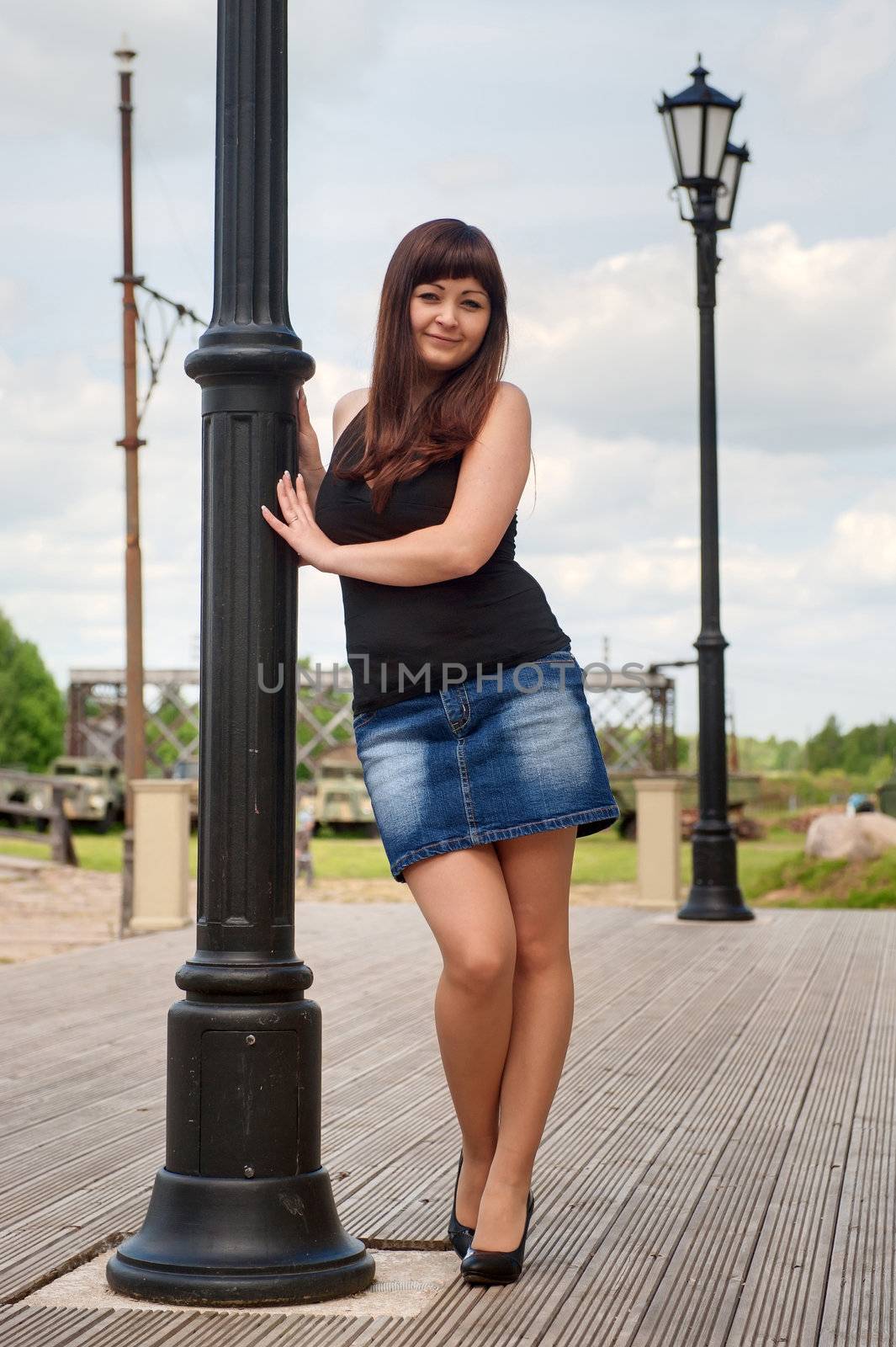 Young, sexy woman in short skirt leans on lantern pillar.