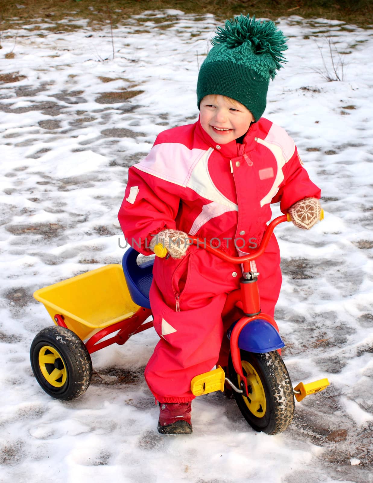 Optimistic child getting her tricycle ready for spring, even though there is still plenty of snow.