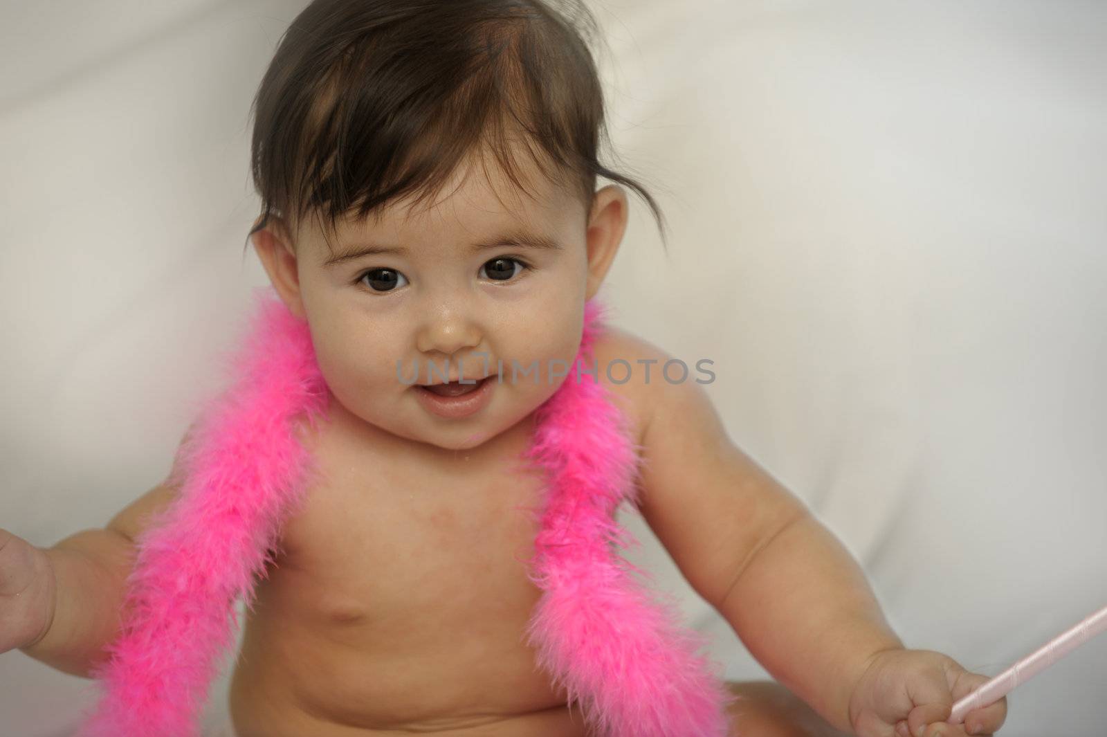 naked baby girl sitting and smiling with pink feather neck wear