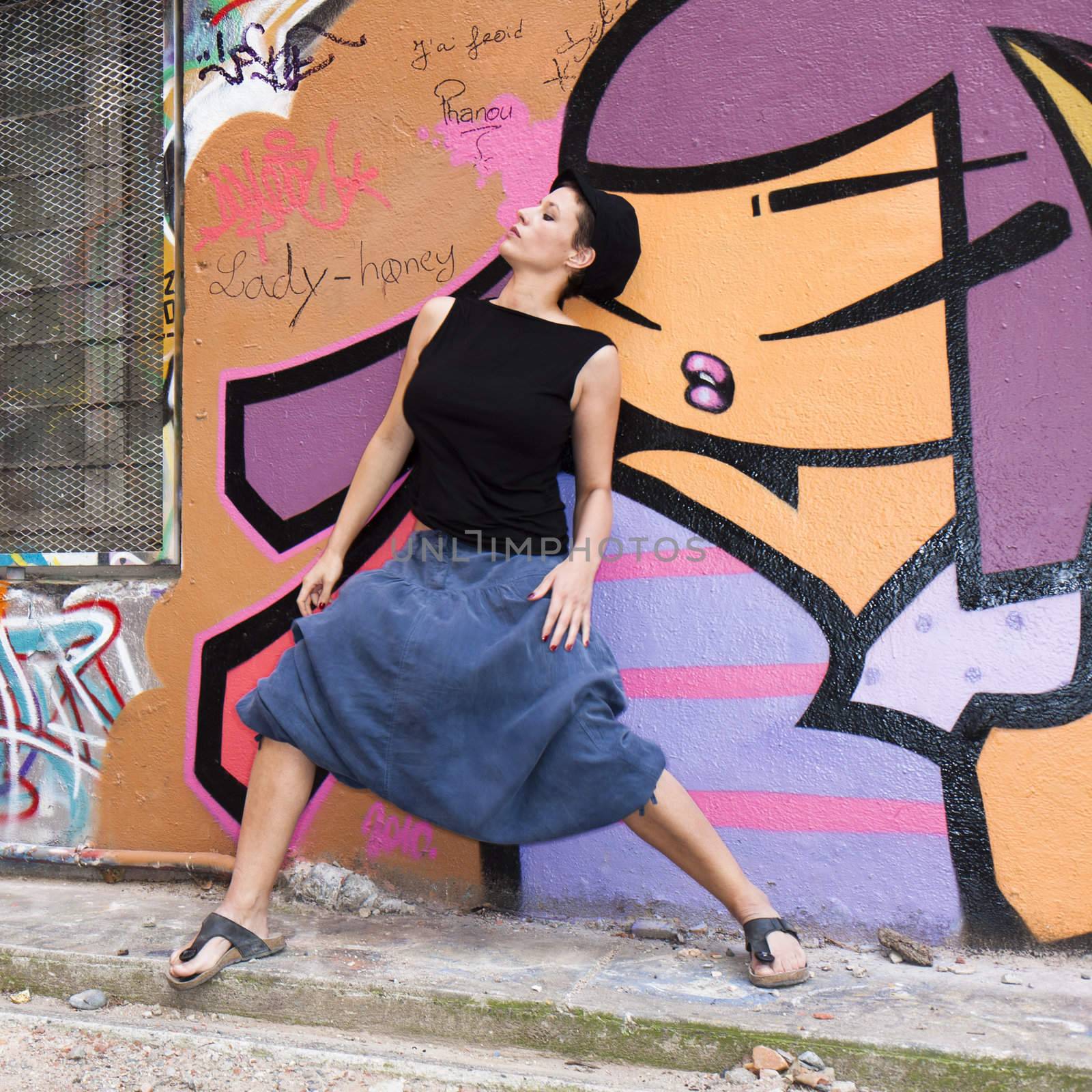 A young woman dancing in front of a wall covered in graffiti