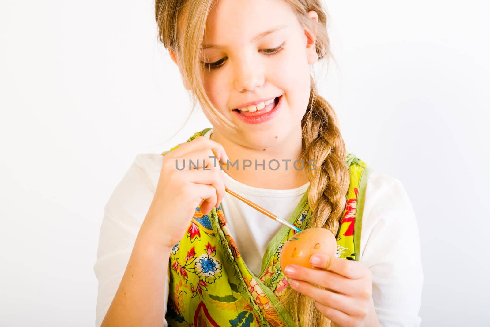 Studio portrait of a young blond girl who ishaving fun painting an easter egg