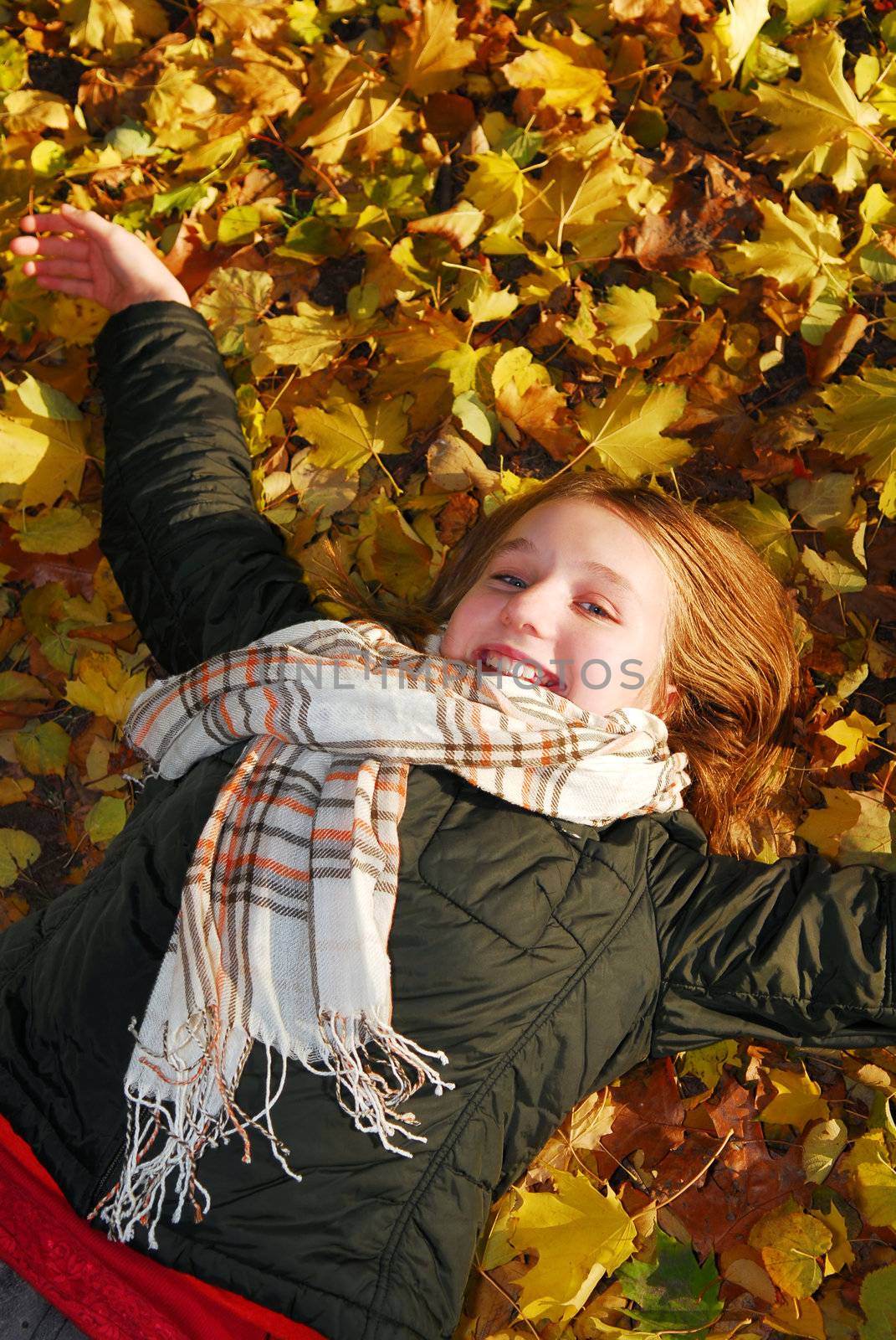 Beautiful teenage girl lying on fallen leaves in autumn park