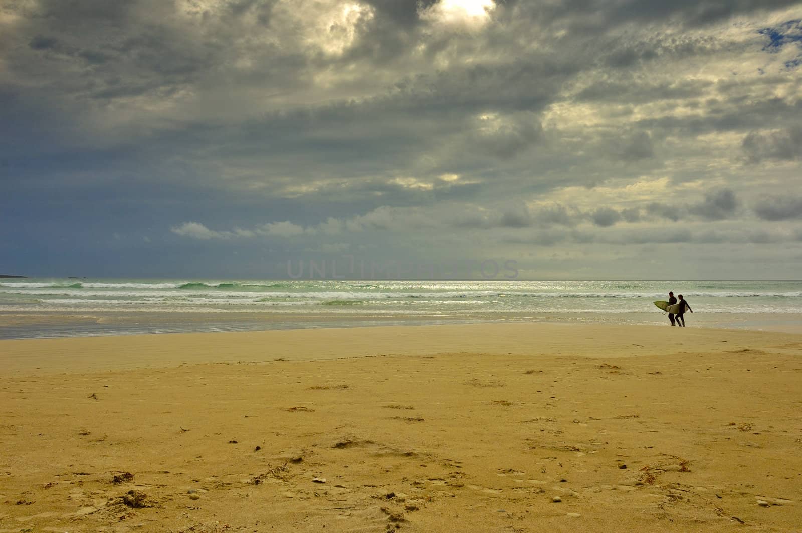 A pair of surfers walk back from the sea before the storm strikes. Space for copy in the sky.