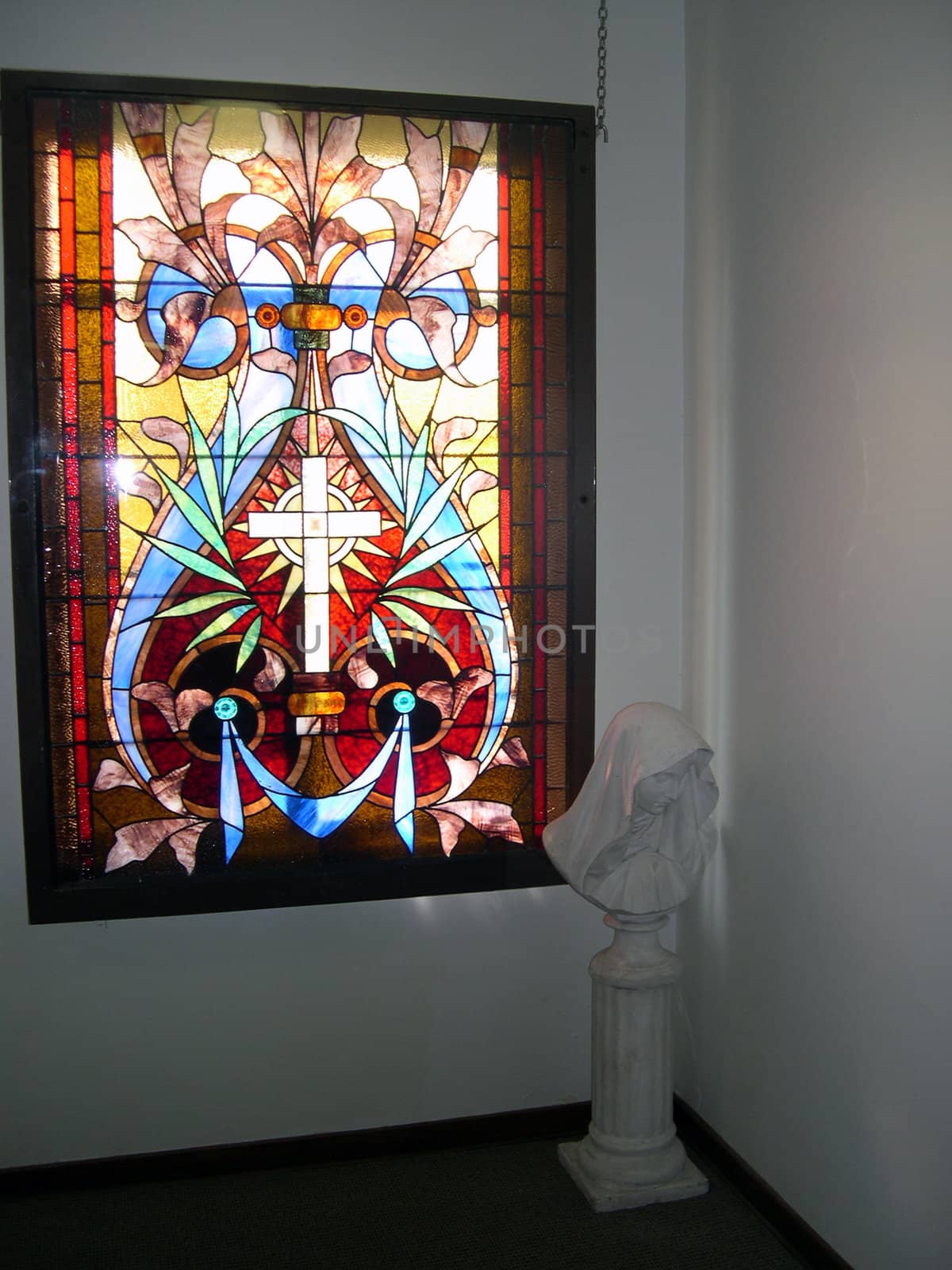 A stained glass window, gently lighting a statue of Mary in a hallway.