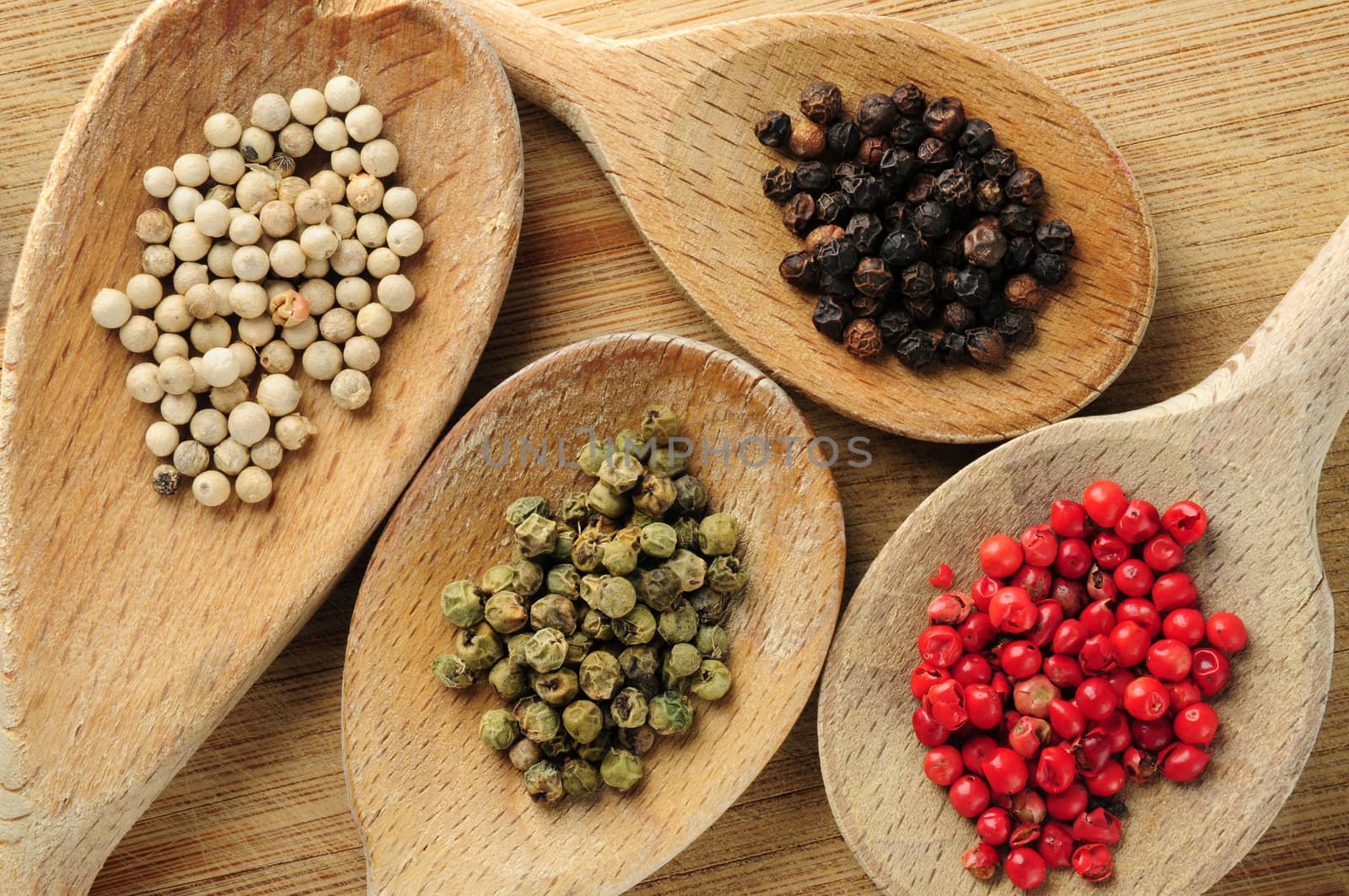 Four kinds of peppercorns in wooden cooking spoons