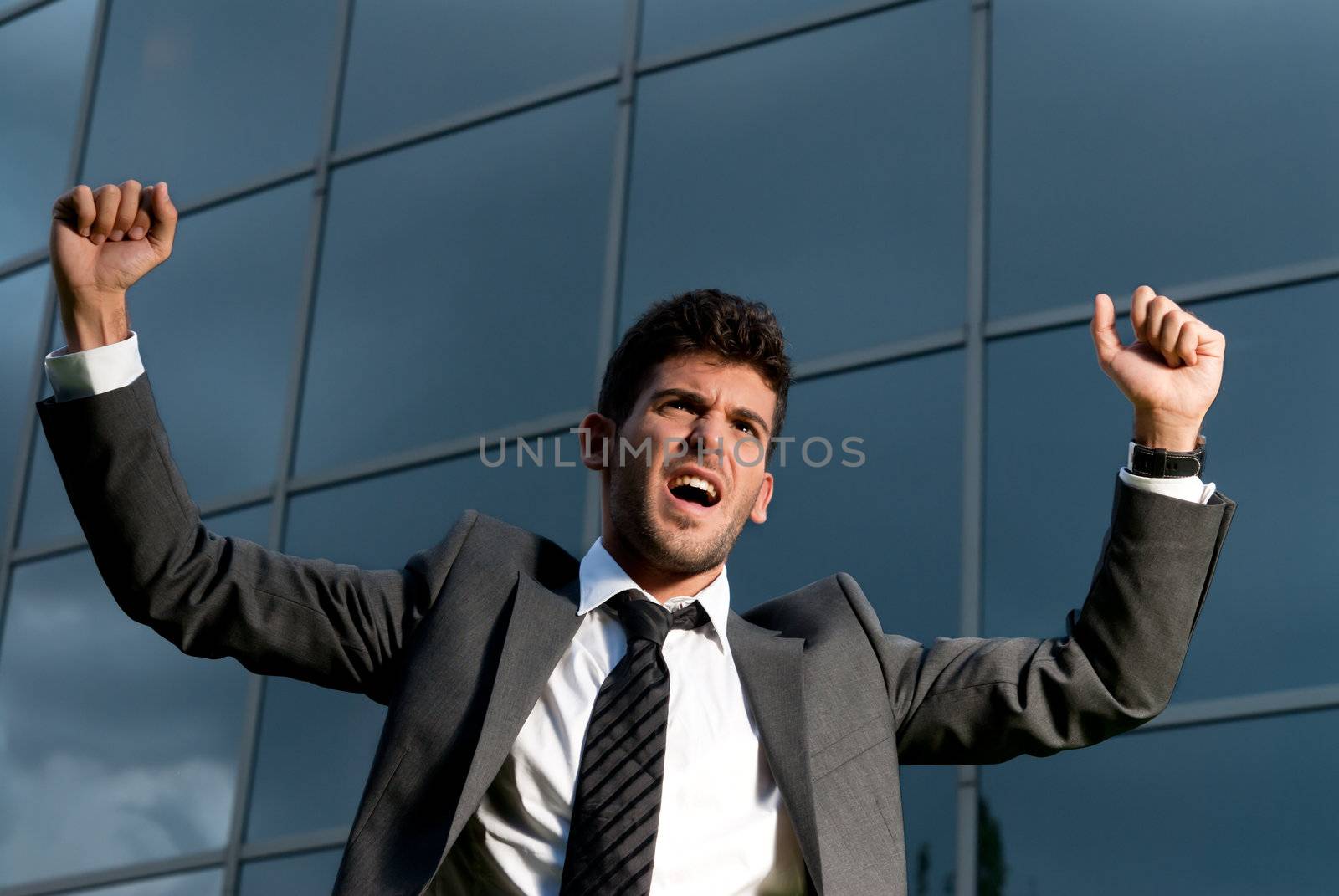 Young successful businessman celebrating a goal on a modern building background by dgmata