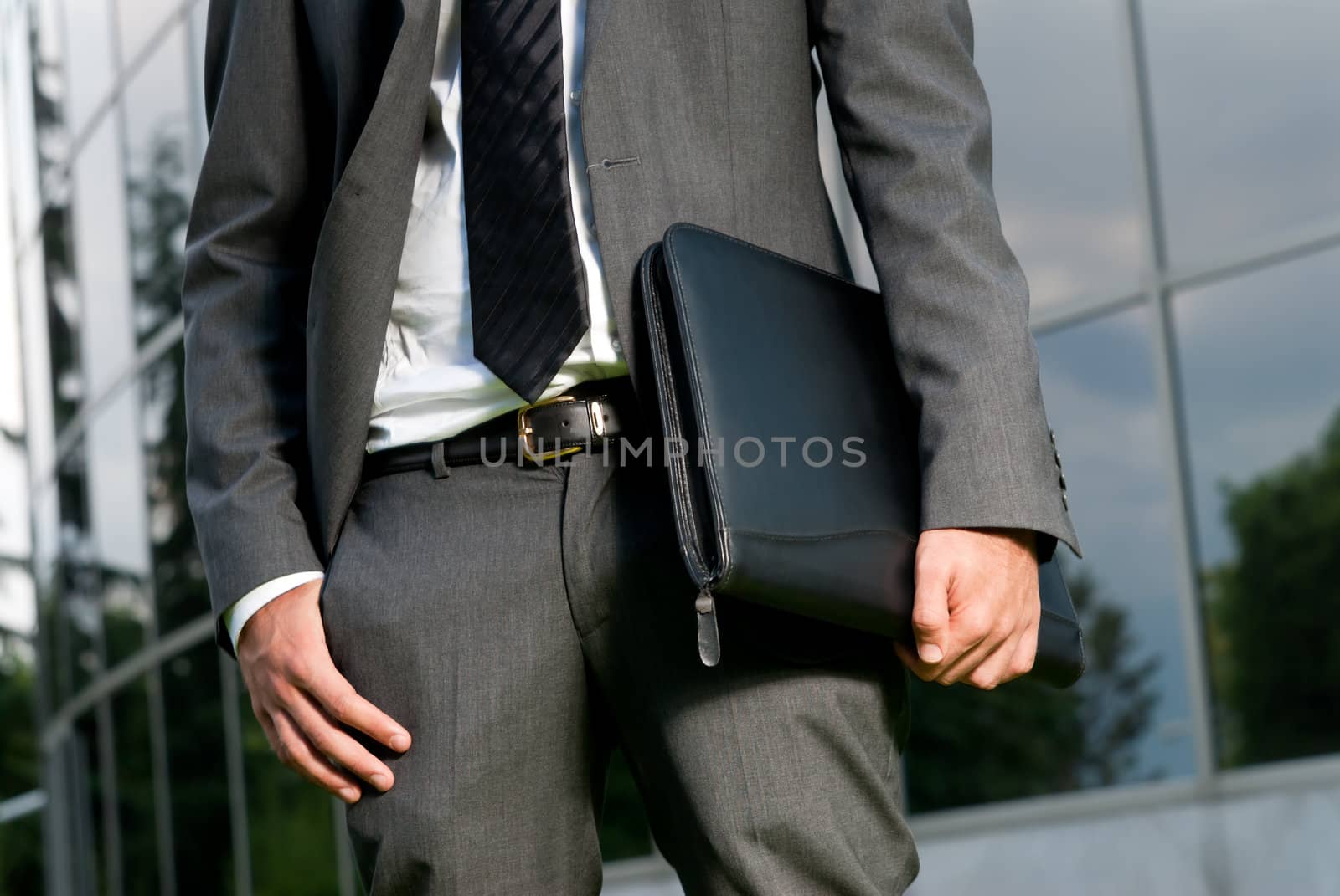 Unrecognizable businessman with suitcase close-up on a modern building background