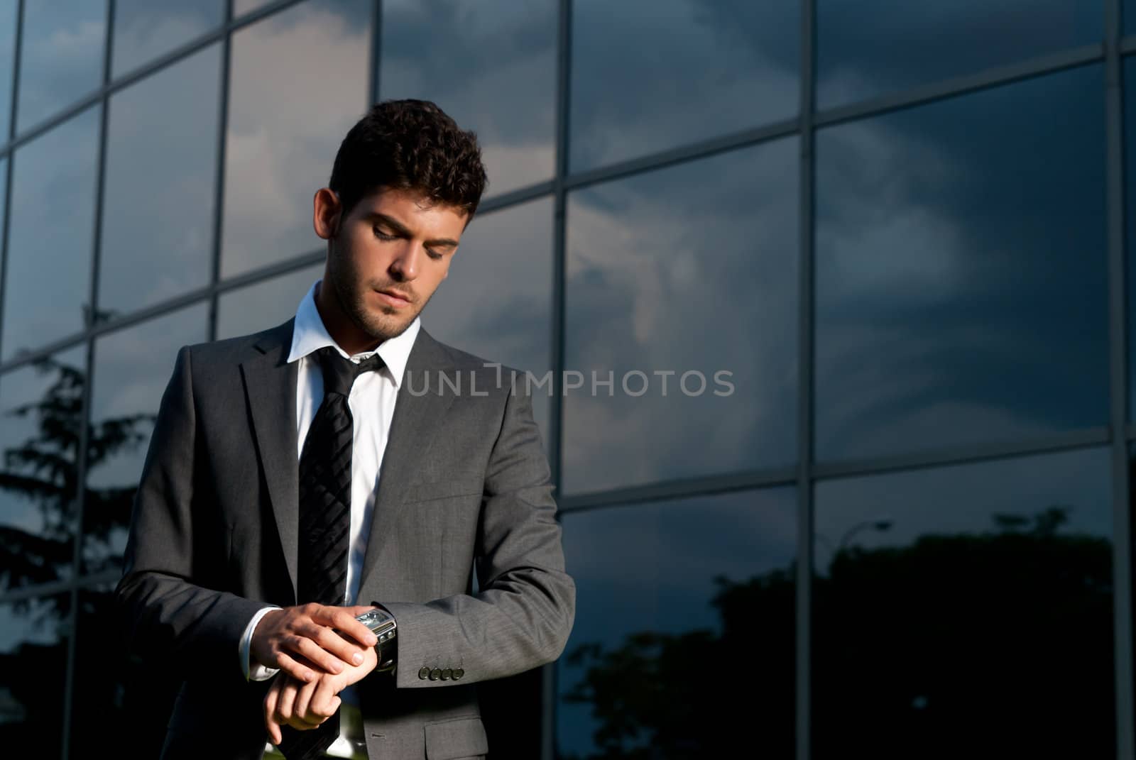 Young businessman looking clock at night on modern building background by dgmata