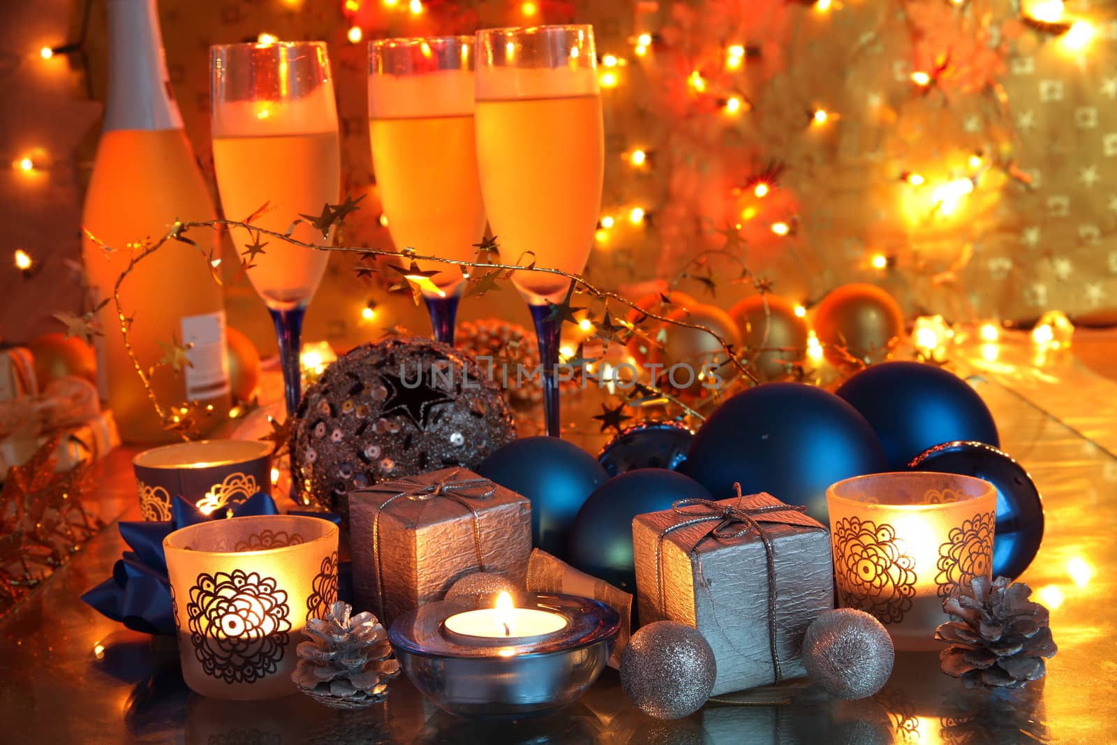 Champagne in glasses,candle lights,gifts,baubles and bluured lights on golden background.